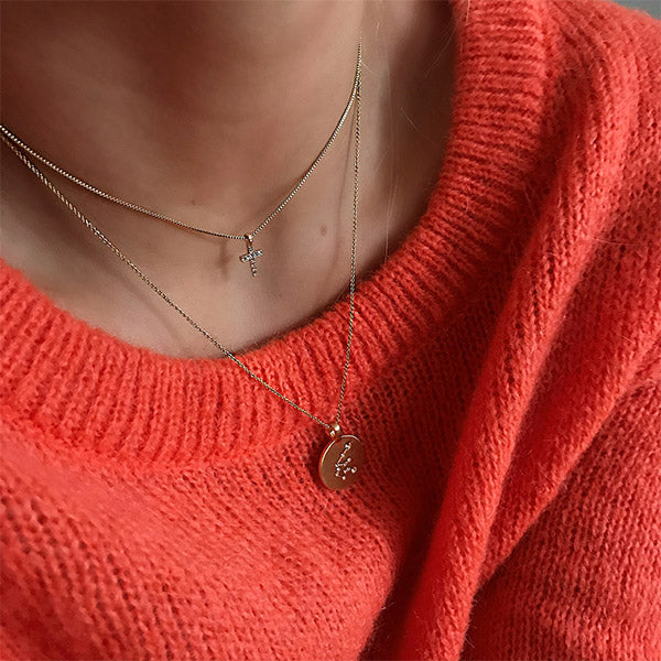 CLARA crystal cross necklace gold-plated on person, featuring a sparkling crystal-adorned cross pendant. The necklace is worn over a sweater.