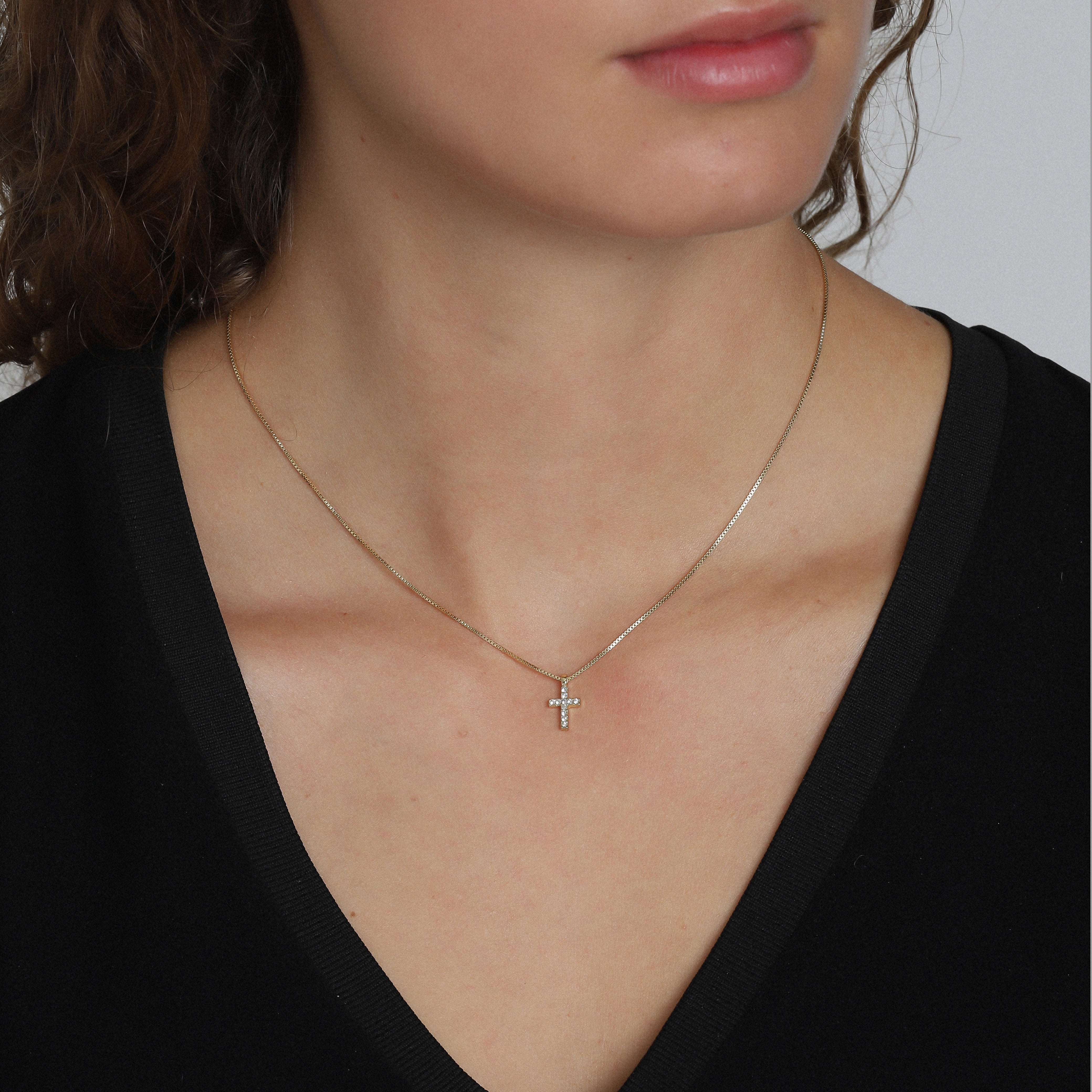 CLARA crystal cross necklace gold-plated, featuring sparkling crystals on a gold-plated chain, elegantly worn by a woman, highlighting its modern and feminine design.