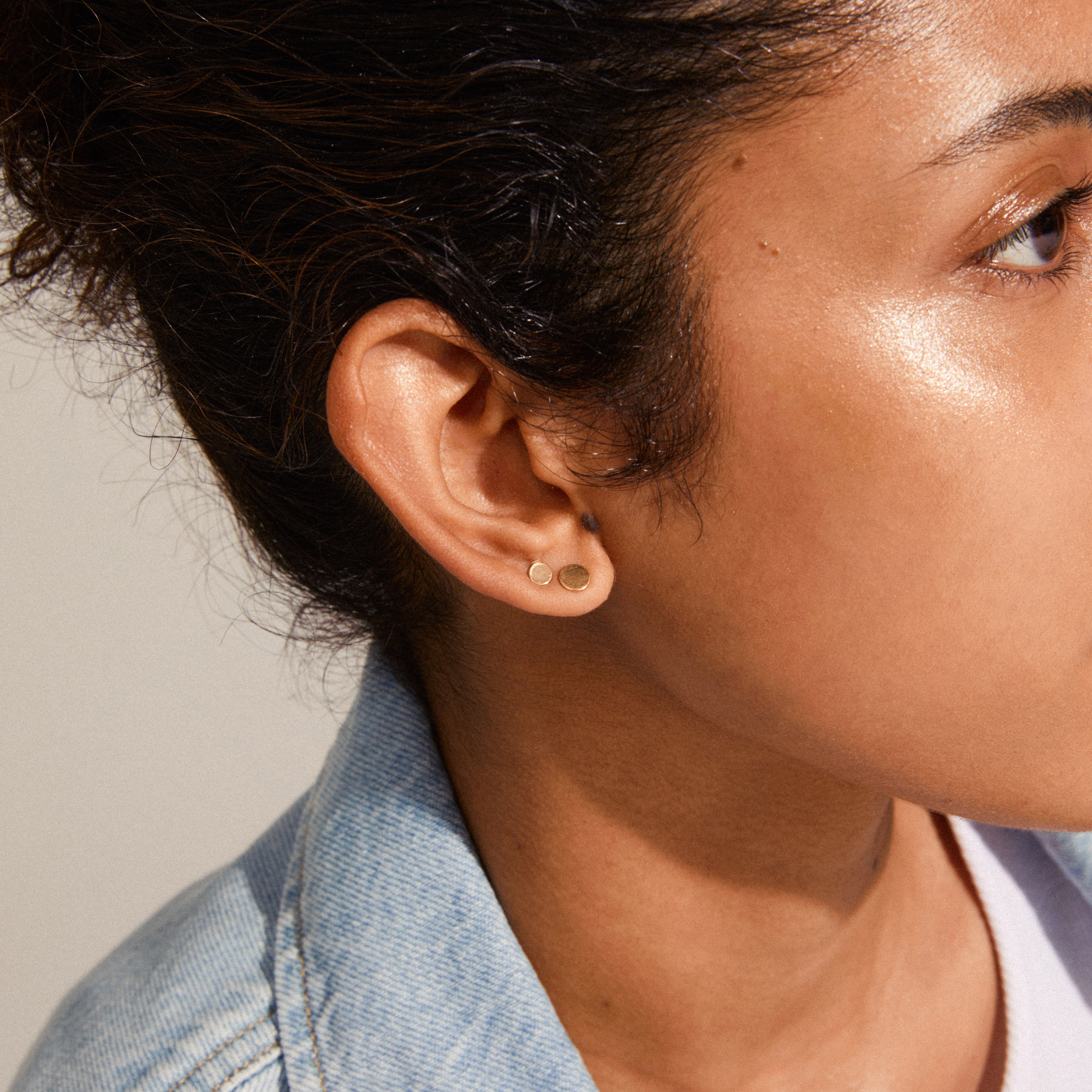 Close-up of a woman's ear wearing NORMA 3-in-1 gold-plated earrings, showcasing minimalist studs in varying sizes for versatile styling.