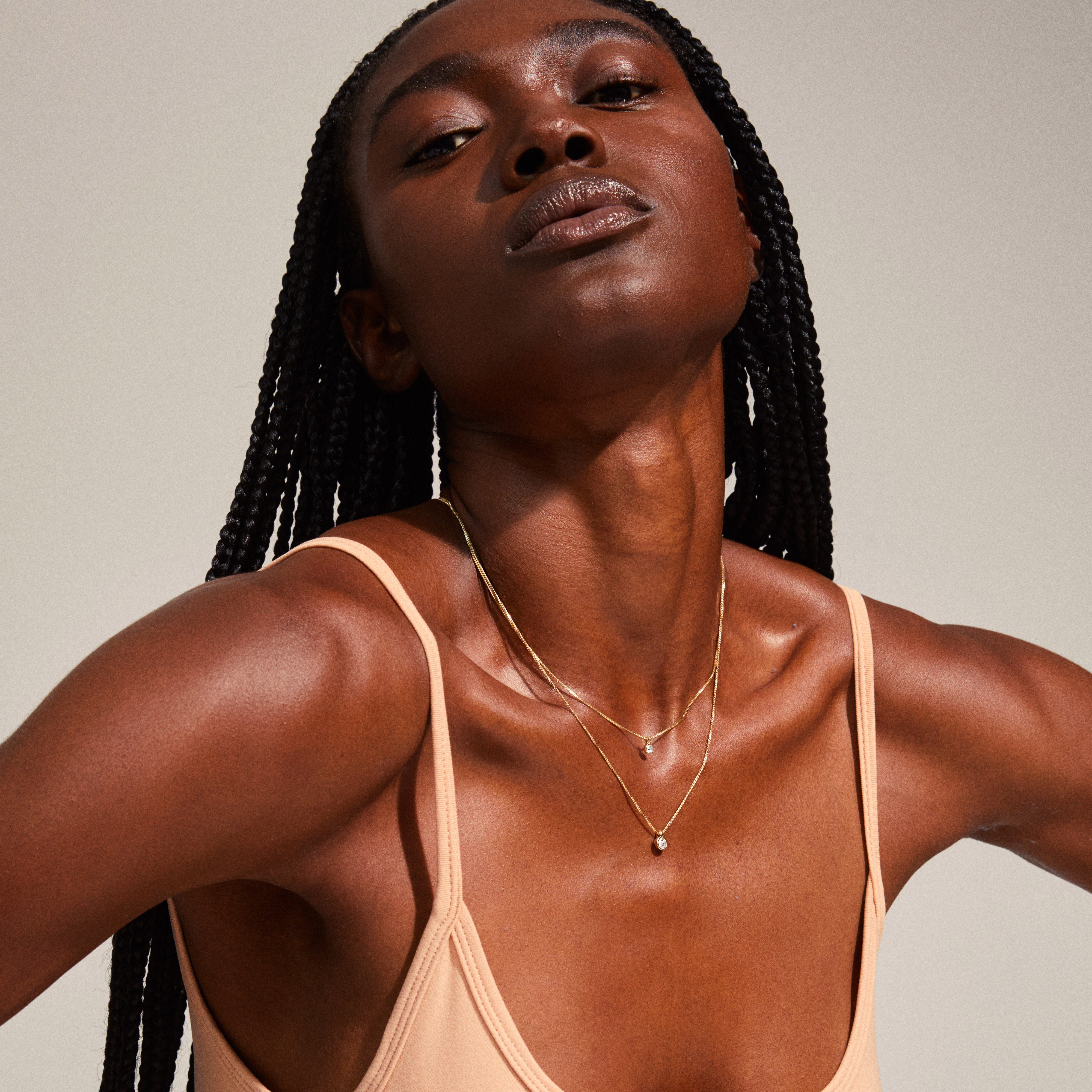 LUCIA 2-in-1 crystal necklace gold-plated, featuring dual chains with sparkling crystal pendants, elegantly displayed on a woman's neck with long black braids.