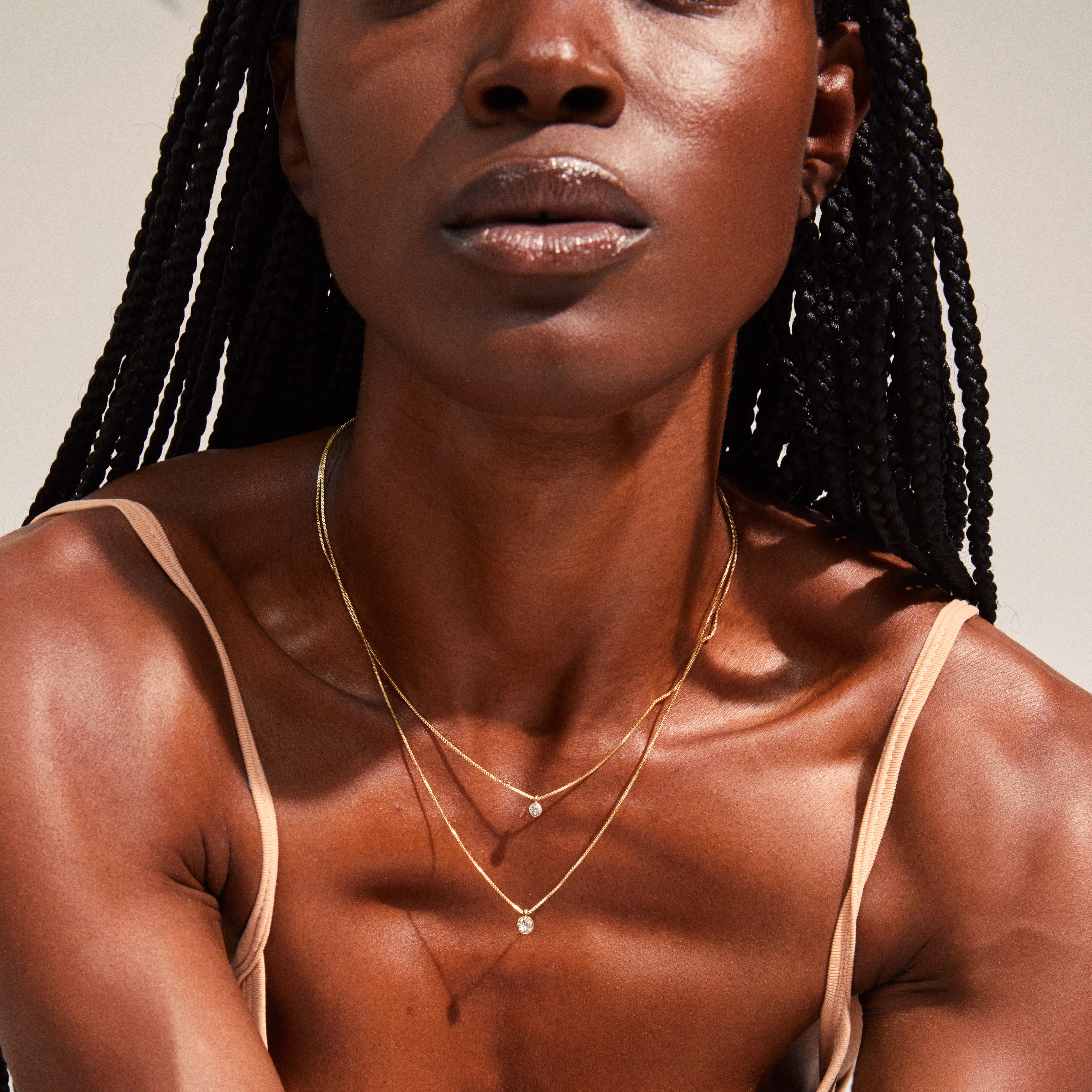 LUCIA 2-in-1 crystal necklace gold-plated worn by a woman with braids, showcasing dual sparkling crystals on layered chains, elegantly resting on her décolleté.