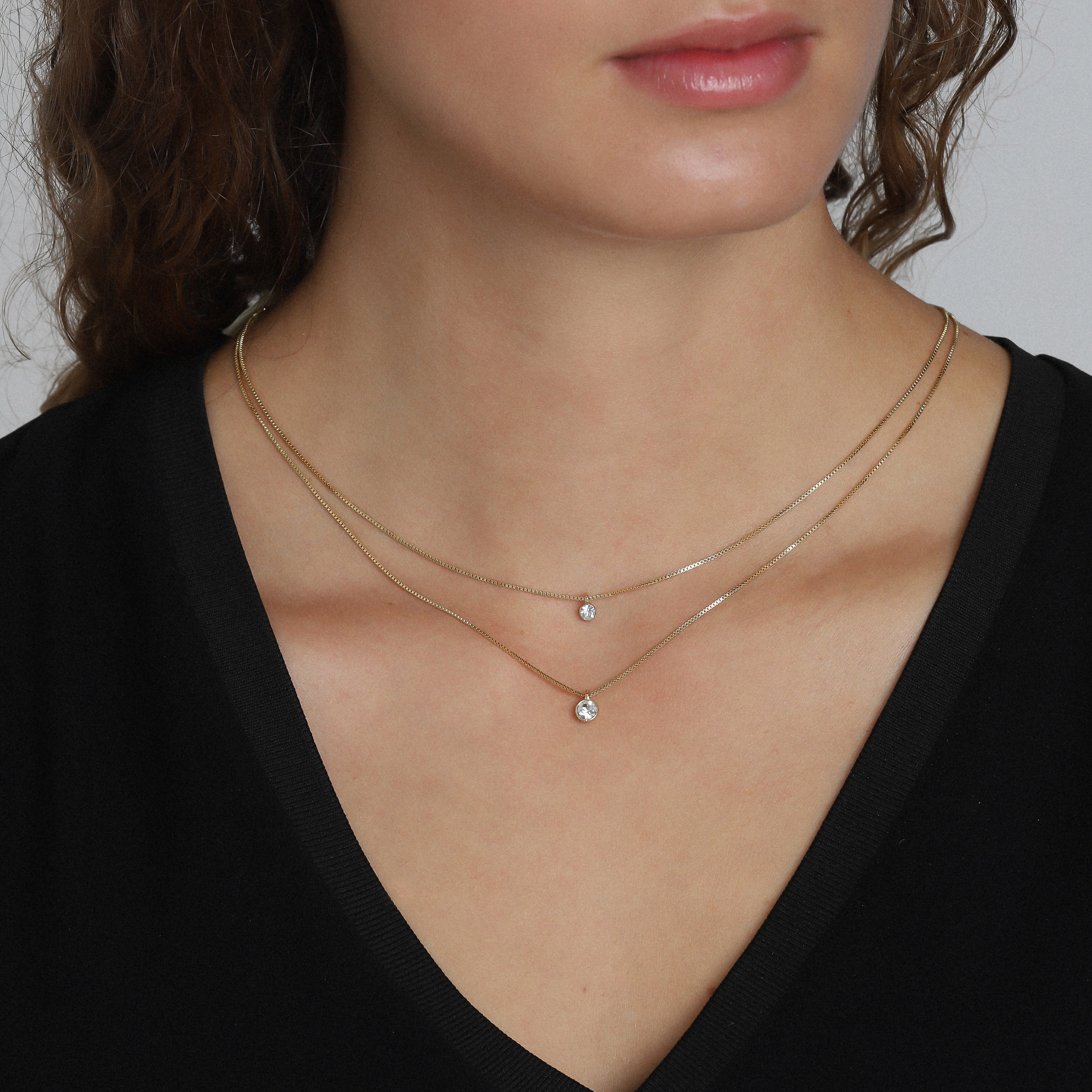 Woman wearing the LUCIA 2-in-1 gold-plated necklace with two sparkling crystal pendants, perfectly layered above her décolleté.
