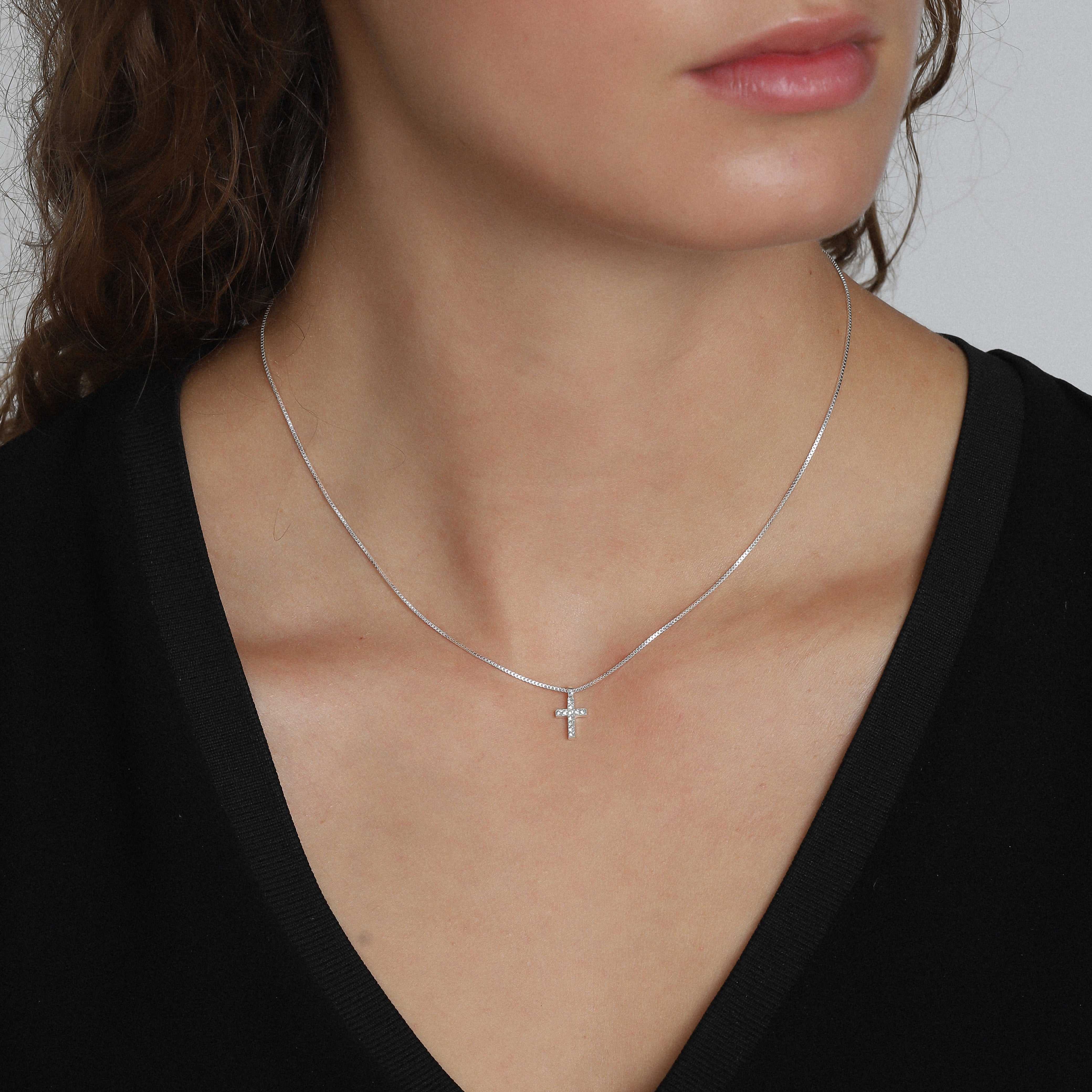 CLARA crystal cross necklace silver-plated, featuring sparkling crystals on a modern cross pendant, worn by a woman, emphasizing its feminine appeal and adjustable chain length.