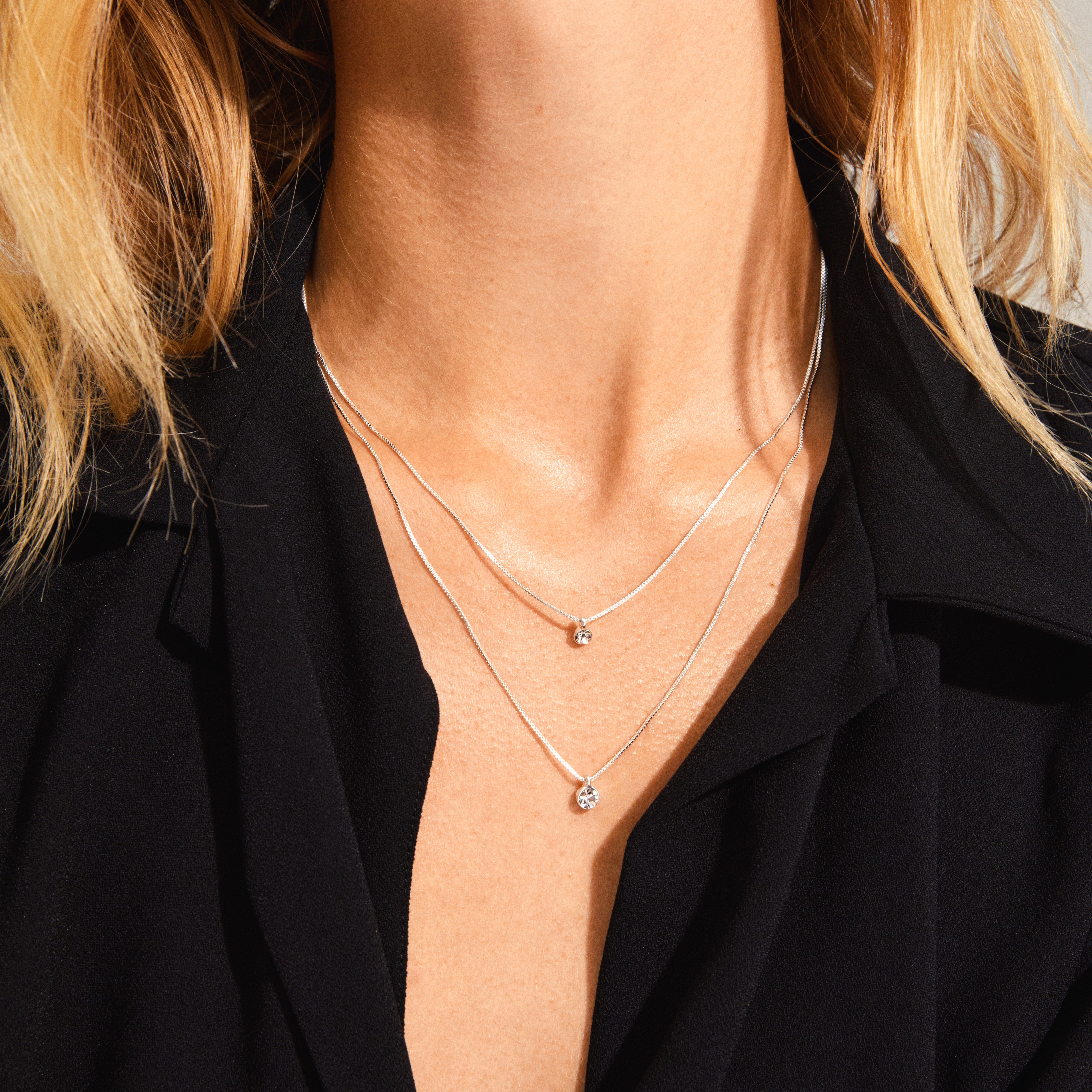 LUCIA 2-in-1 crystal necklace silver-plated, featuring dual crystal pendants on layered chains, elegantly adorns a woman's neck.