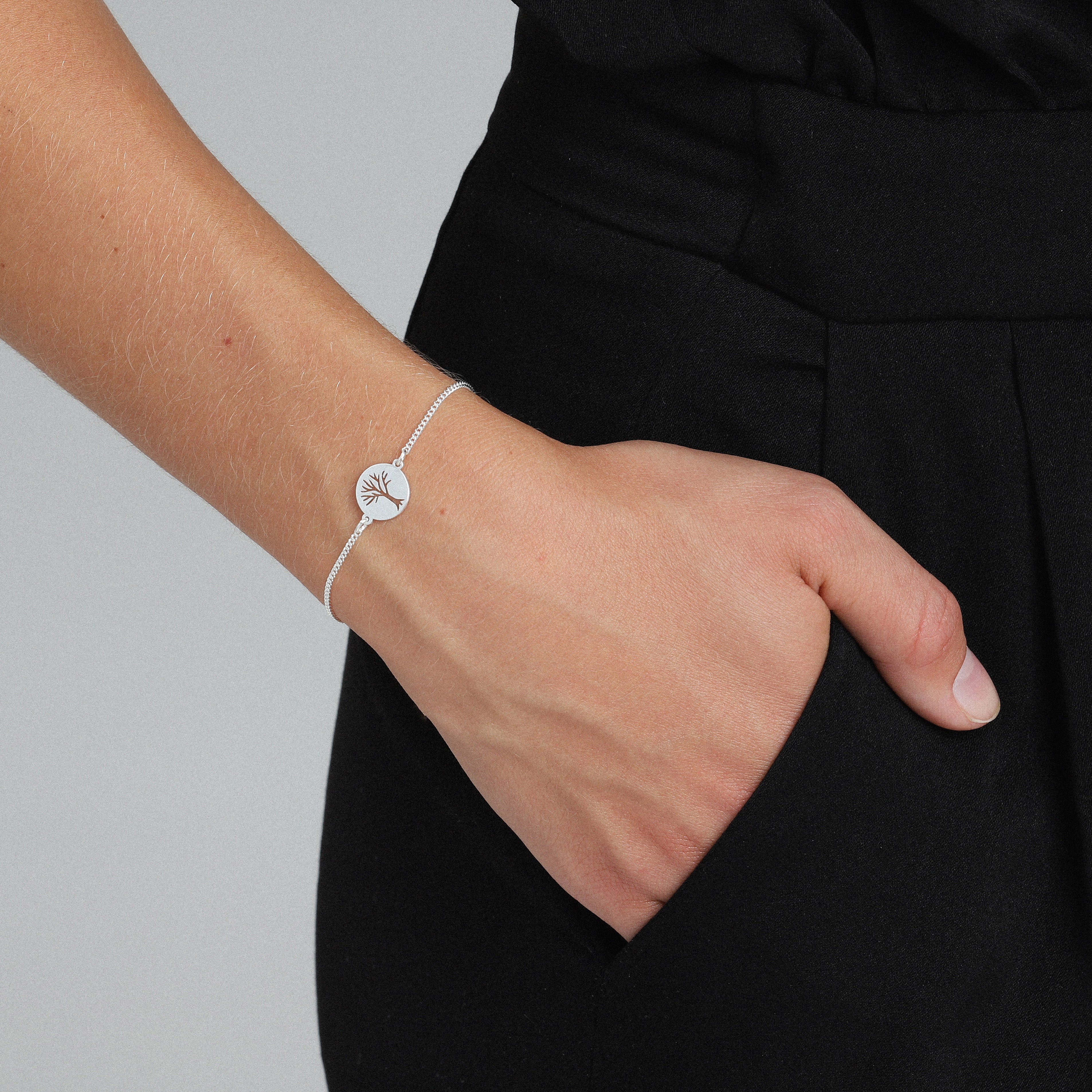 Person wearing the ELIN coin bracelet, a silver-plated accessory featuring a delicate chain and a circular pendant with an etched tree motif.