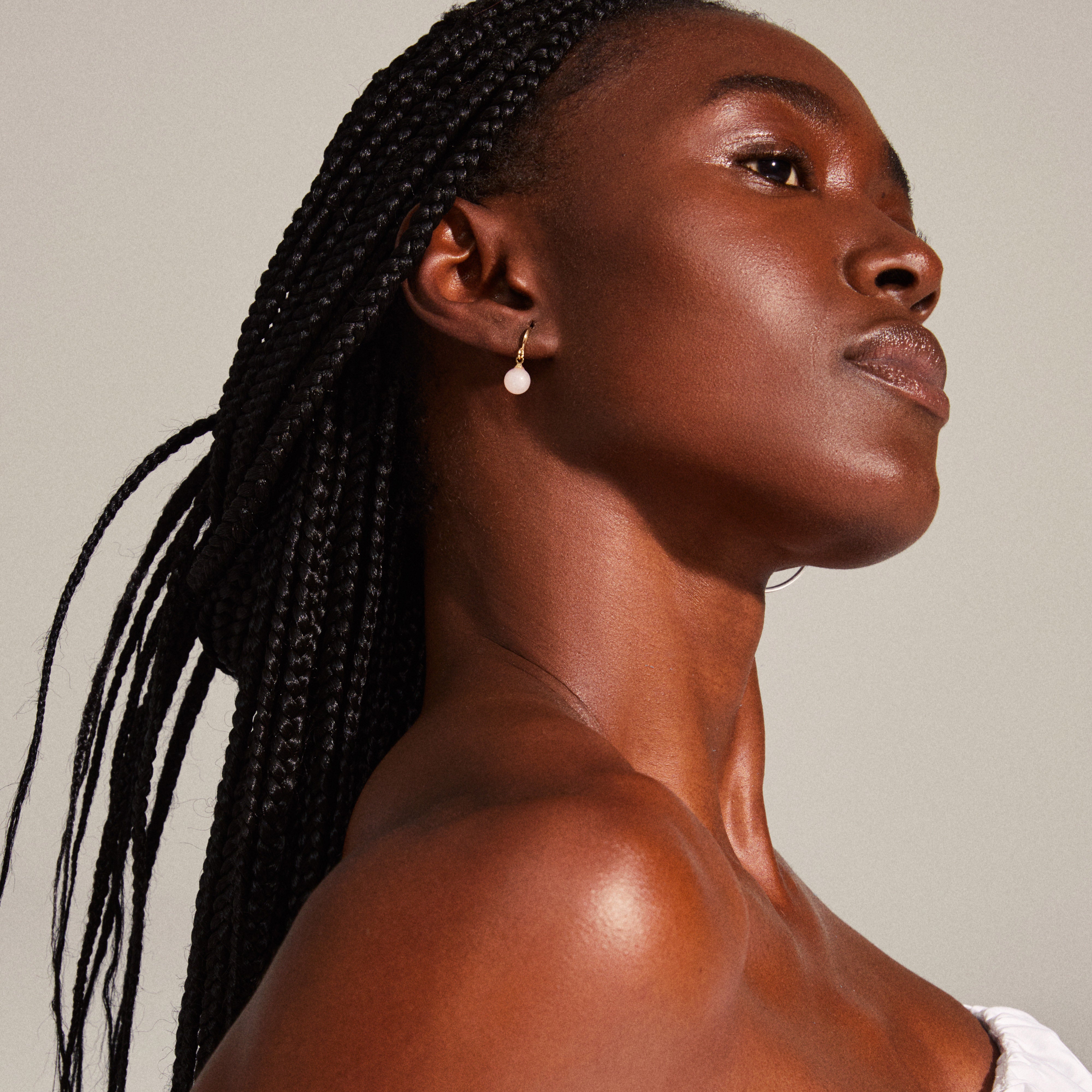 GOLDIE pink earrings gold-plated, featuring gold hooks and pink-tinted glass beads, worn by a woman with braided hair, showcasing elegance and style.