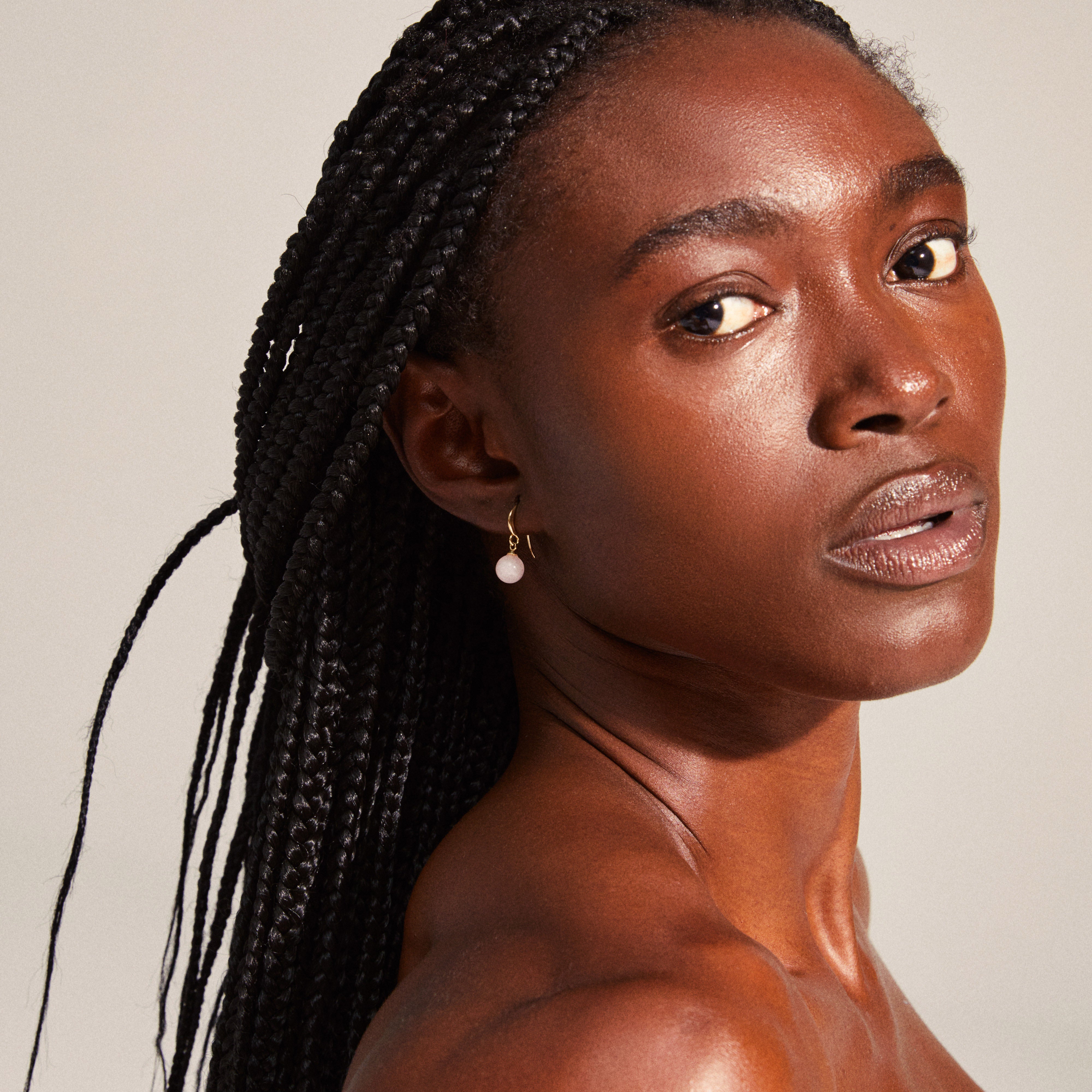 GOLDIE pink earrings, gold-plated, featuring pink-tinted glass beads. Worn by a woman with long braids, showcasing the elegant design and delicate craftsmanship.