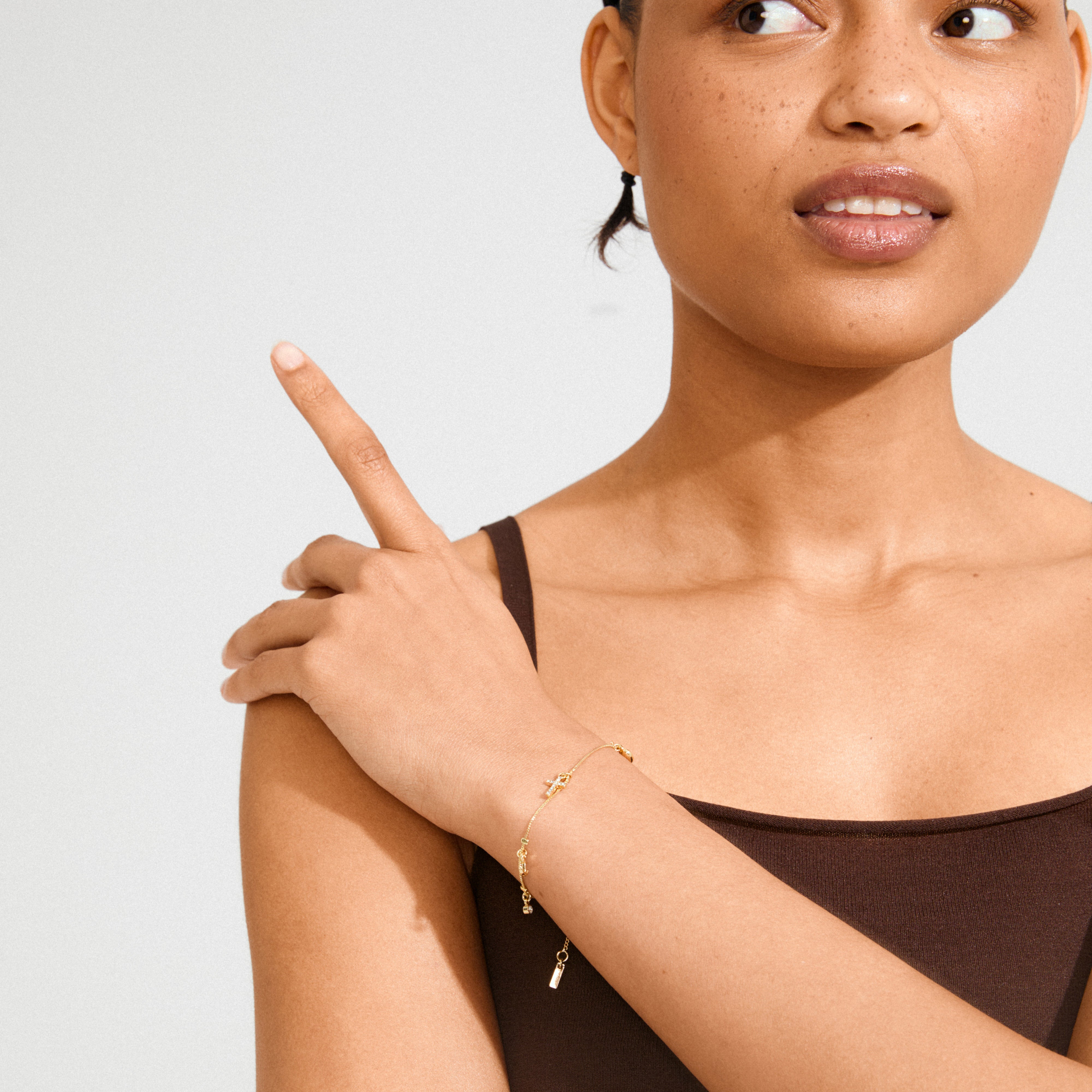 Woman wearing ANET crystal bracelet gold-plated, featuring pendants symbolizing faith, hope, and love, with sparkling Preciosa crystals, resting her hand on her shoulder.