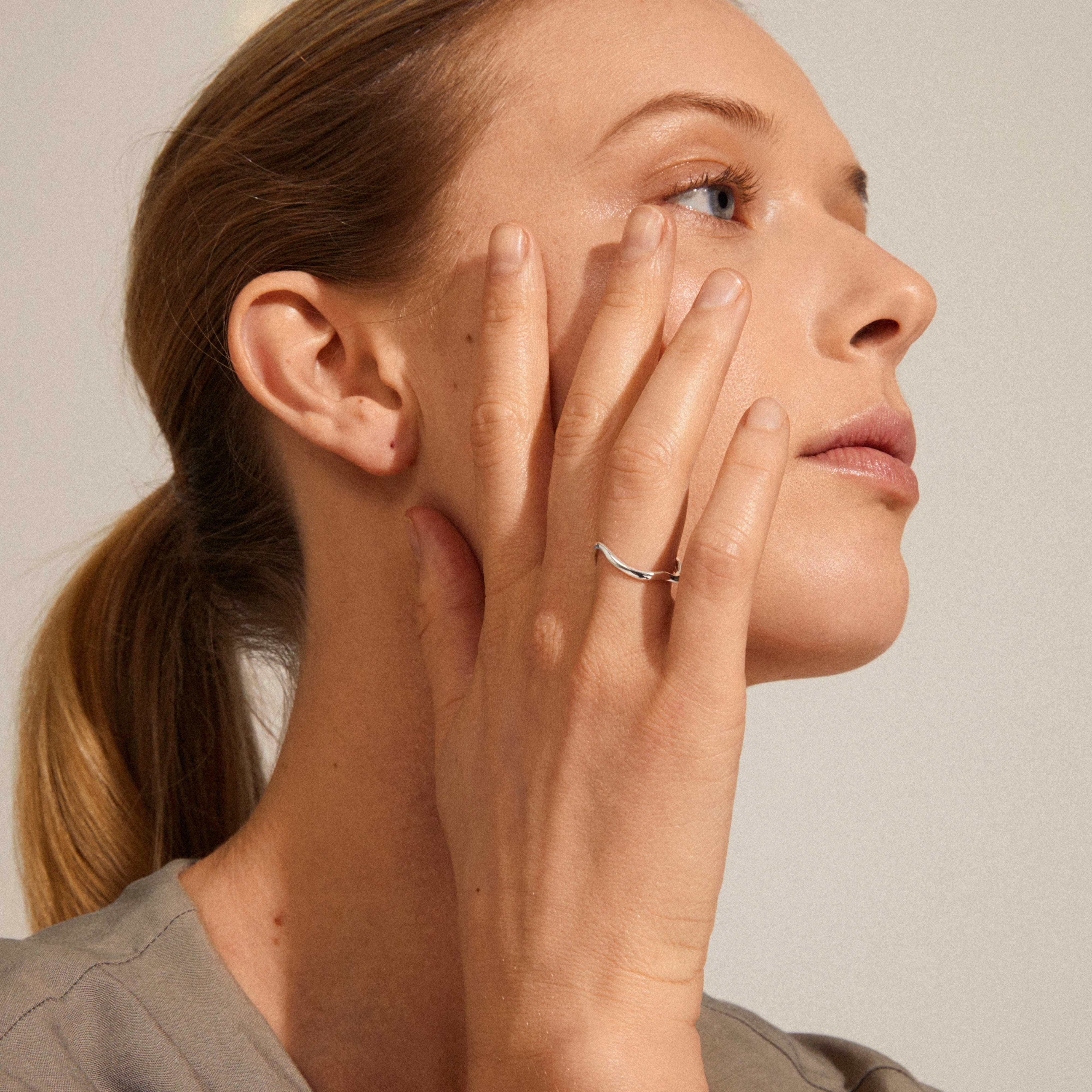 Woman wearing ALBERTE organic shape ring, silver-plated, showcasing its handcrafted, wavy design inspired by the sea, adding elegance to her look.