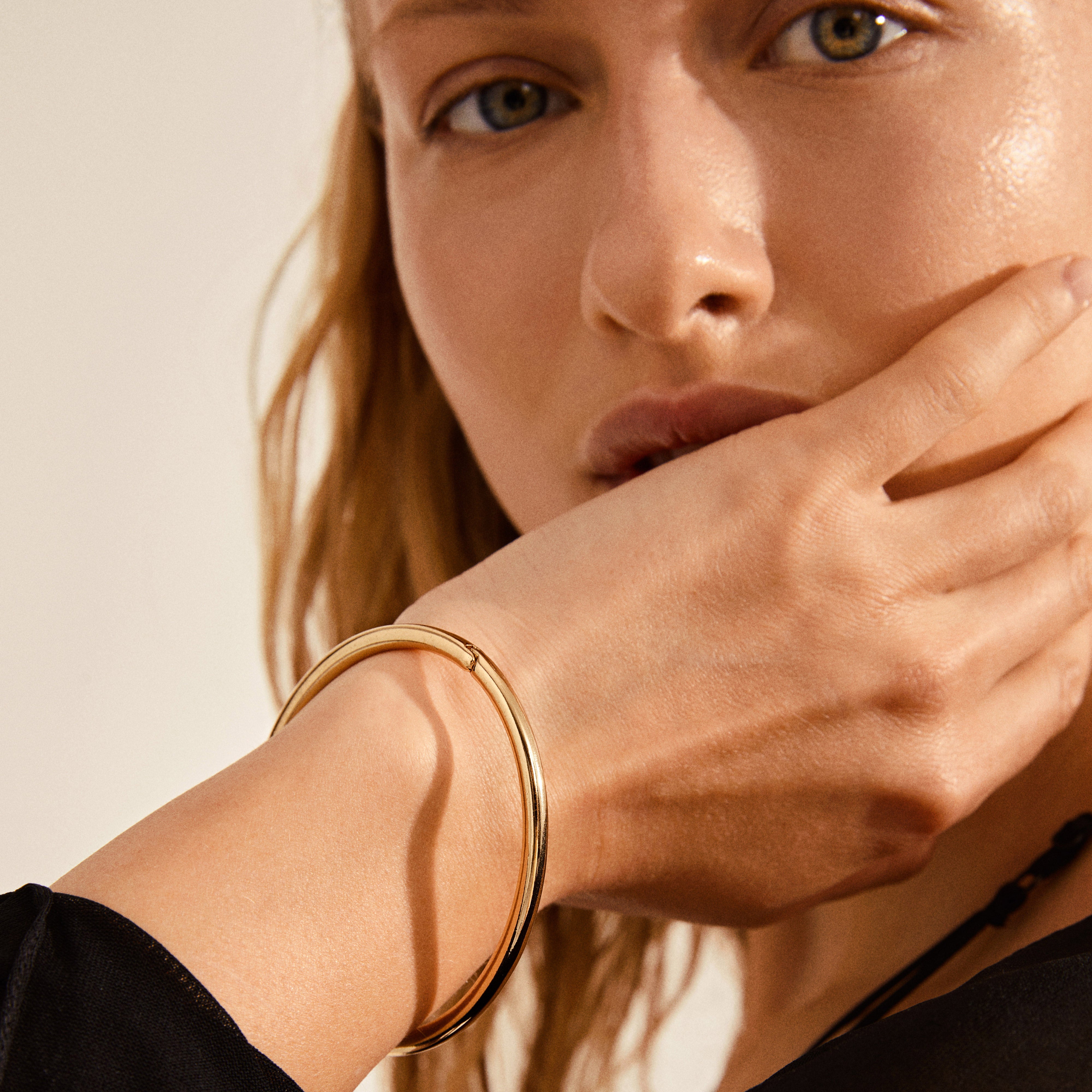 Close-up of a woman wearing the SOPHIA gold-plated bangle bracelet by Pilgrim, showcasing its elegant, shiny surface and classic design.