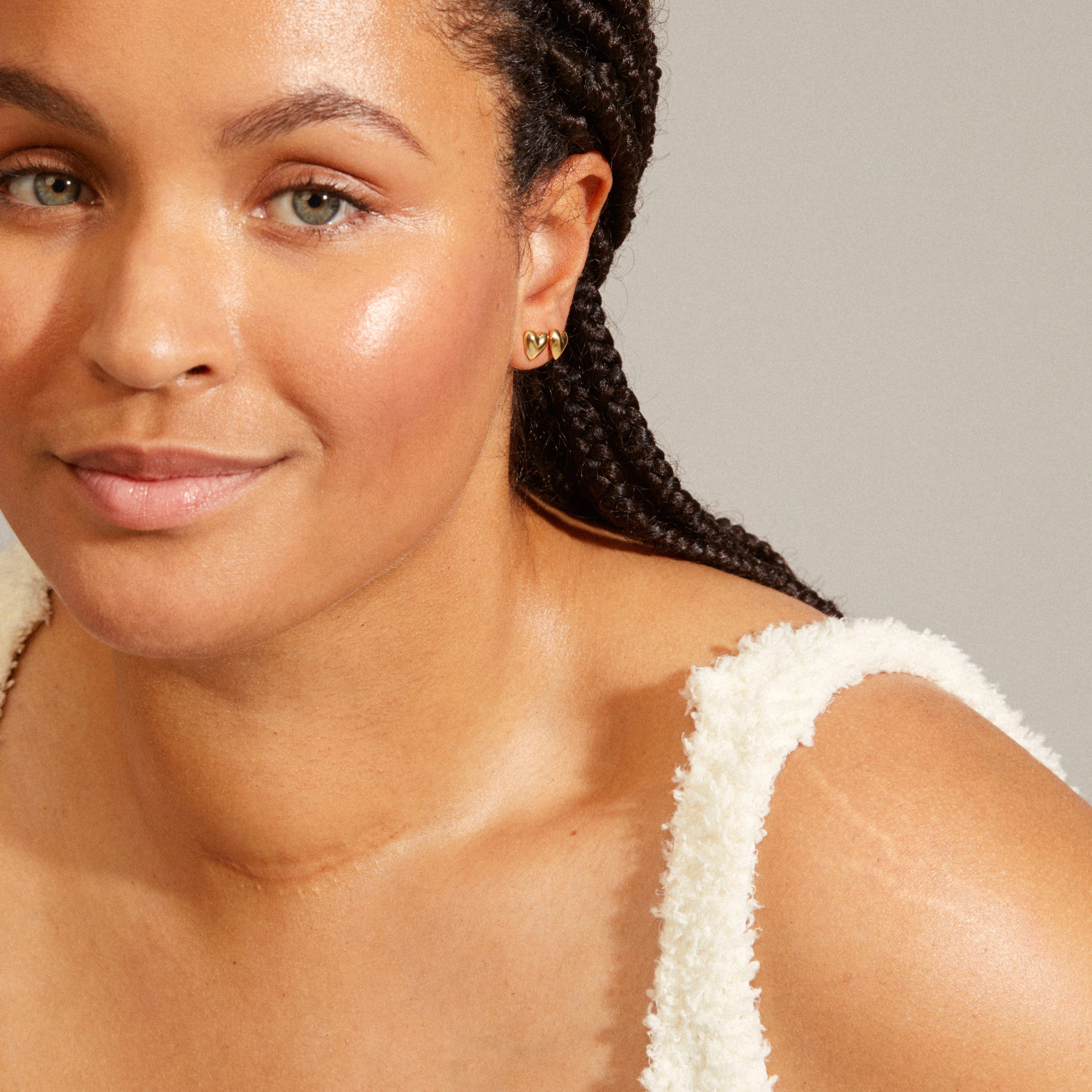 SOPHIA heart earrings, gold-plated, worn by a woman with long black braids. Elegant, shiny, recycled design complementing her white dress.