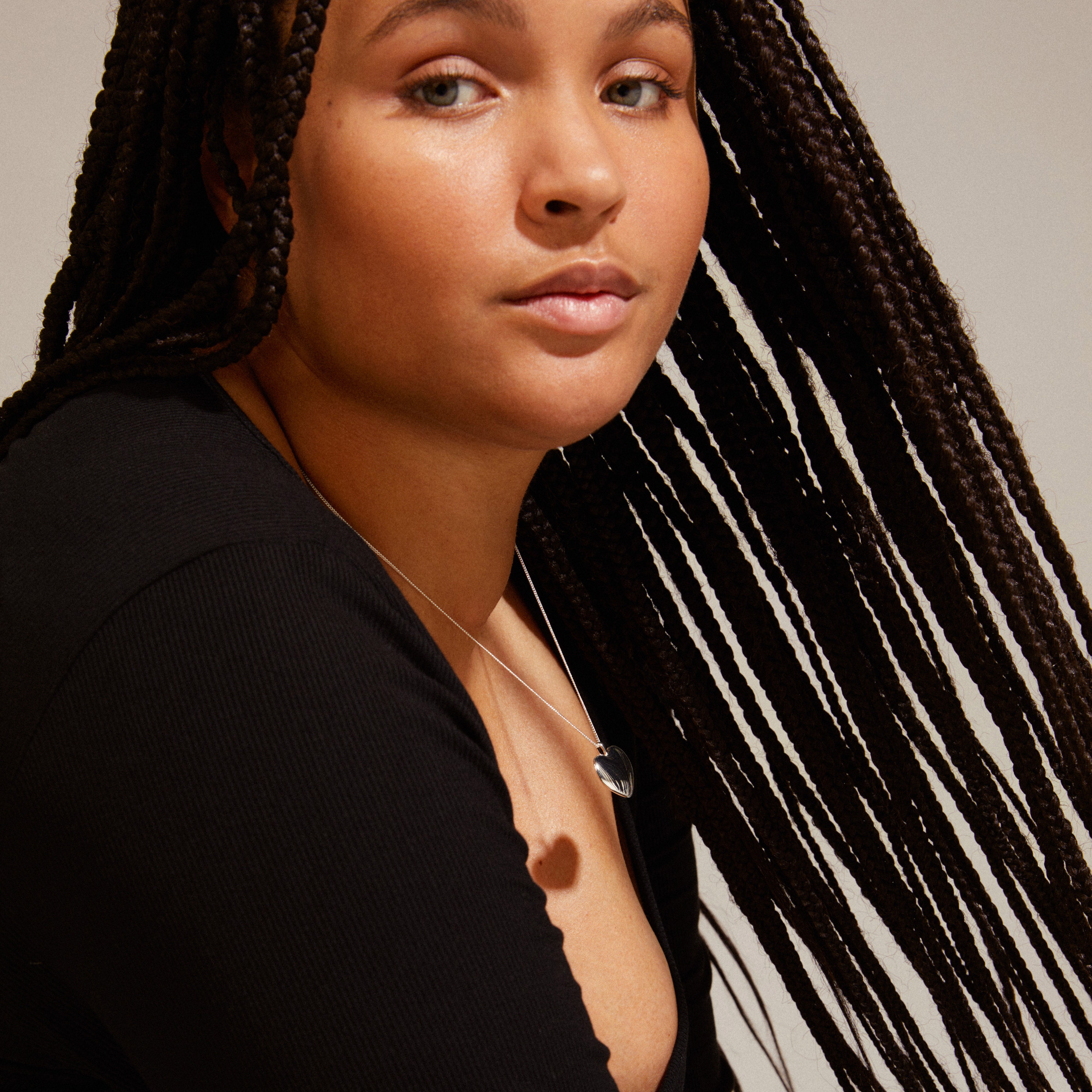 SOPHIA heart pendant necklace silver-plated worn by woman with long braids, showcasing its elegant, shiny design. Ideal for a timeless, stylish look.