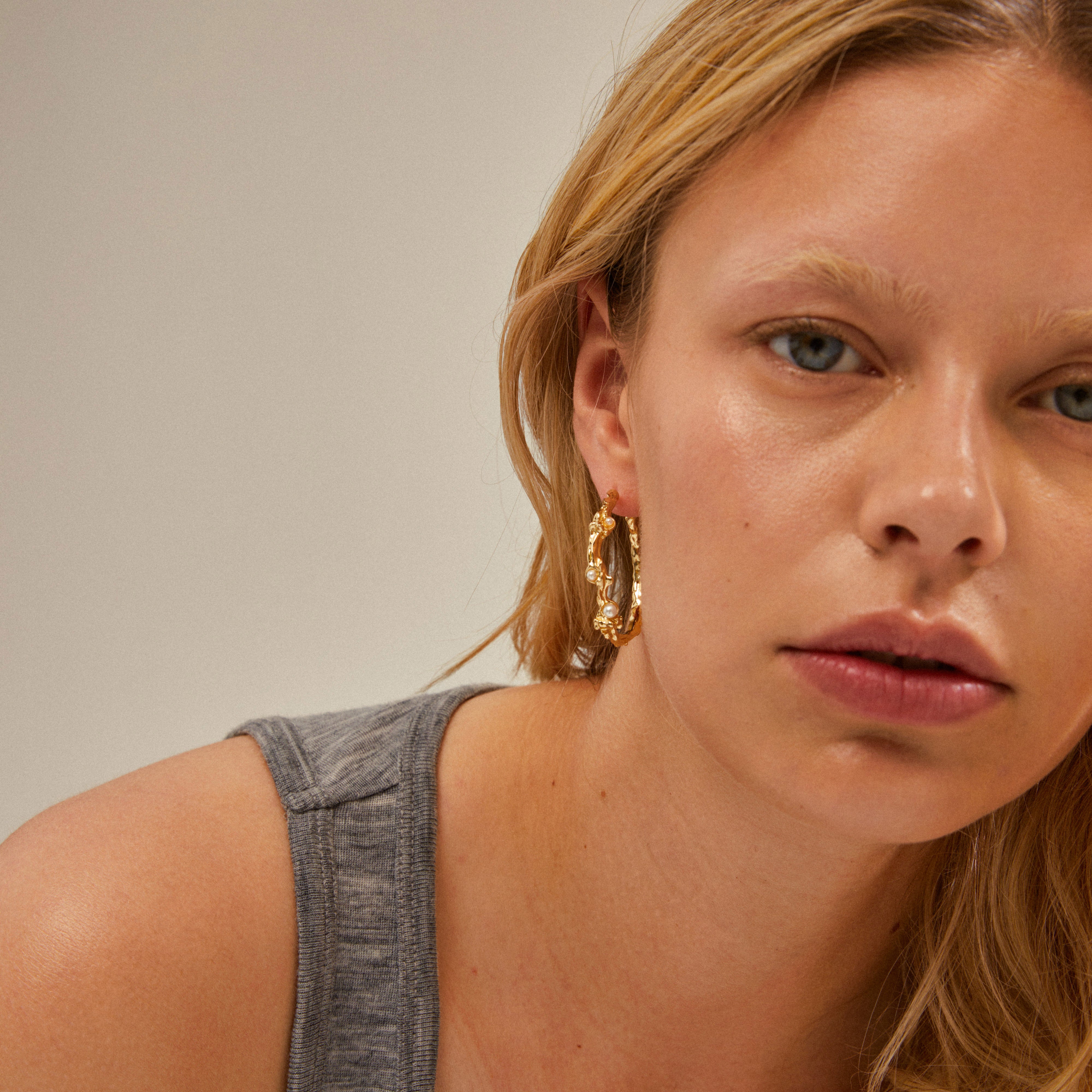 Close-up of a woman wearing RAELYNN gold-plated hoops with white beads, showcasing their organic, handcrafted design.