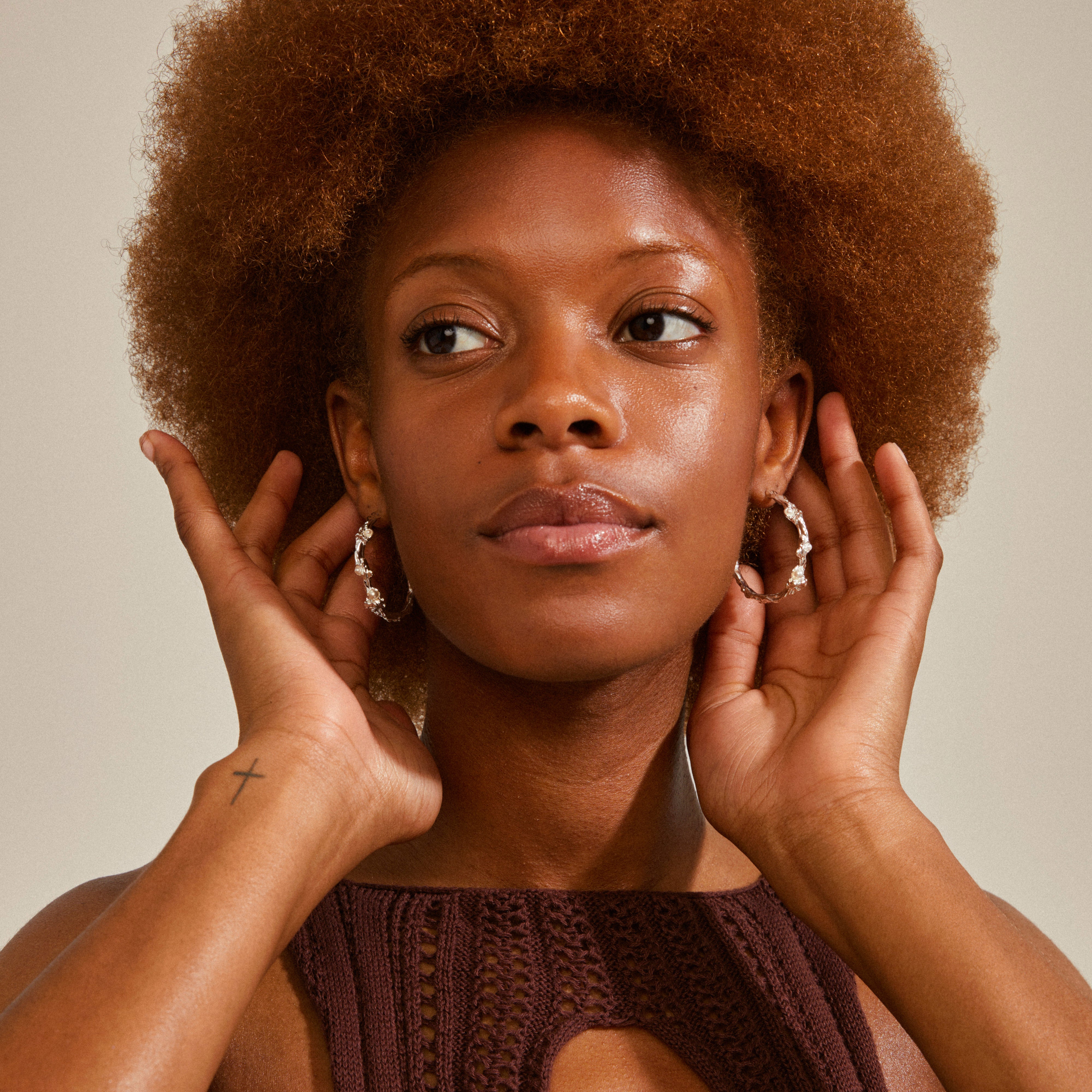 A woman with curly hair wears silver-plated RAELYNN hoops from Pilgrim, featuring an organic design with white beads, embodying a chic, handcrafted style.