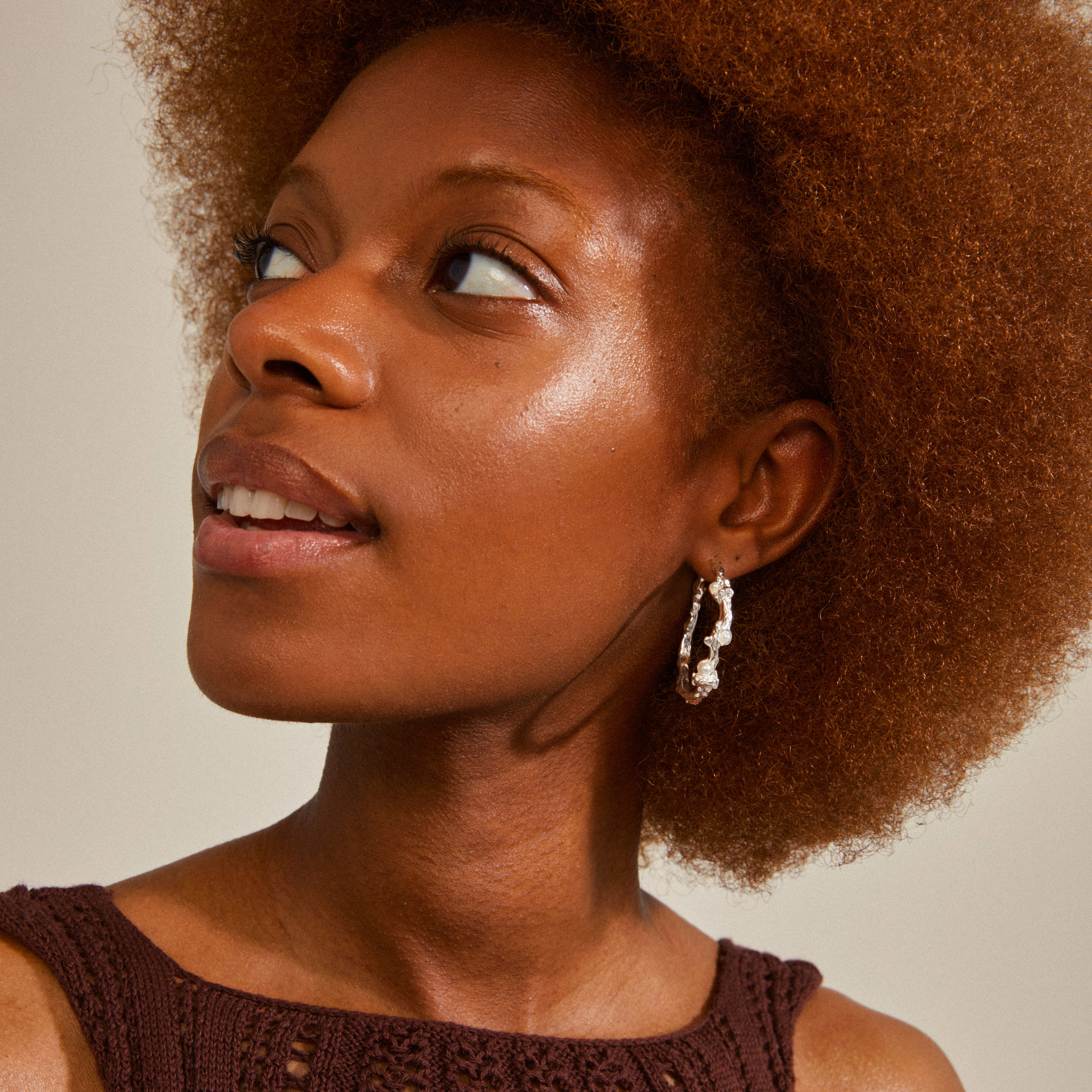 RAELYNN hoops silver-plated earrings by Pilgrim, featuring an organic design with small white beads, worn by a woman gazing upwards.