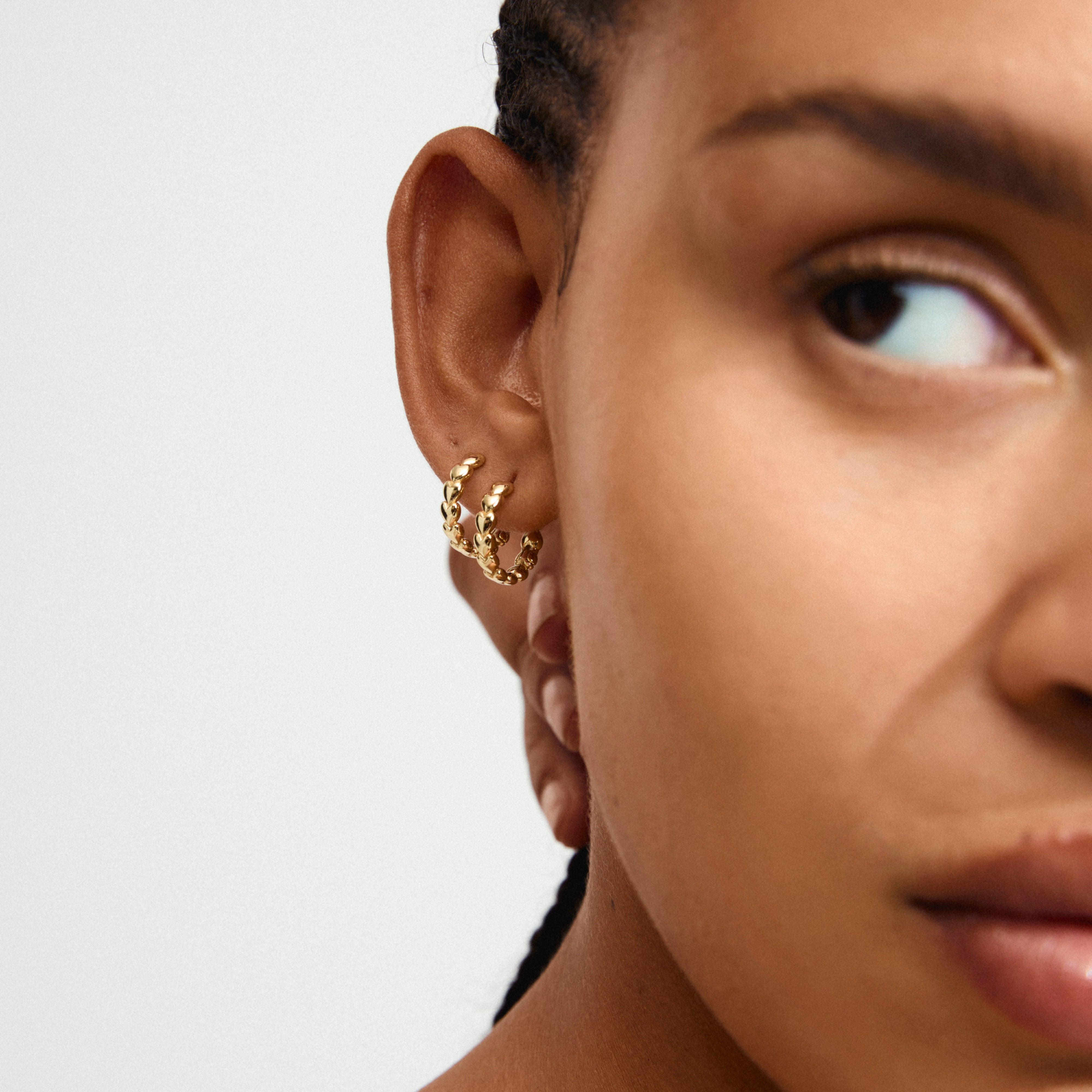 MAEVE hoop earrings gold-plated with heart design on a woman's ear, showcasing elegant craftsmanship and versatile style from Pilgrim's timeless jewelry collection.