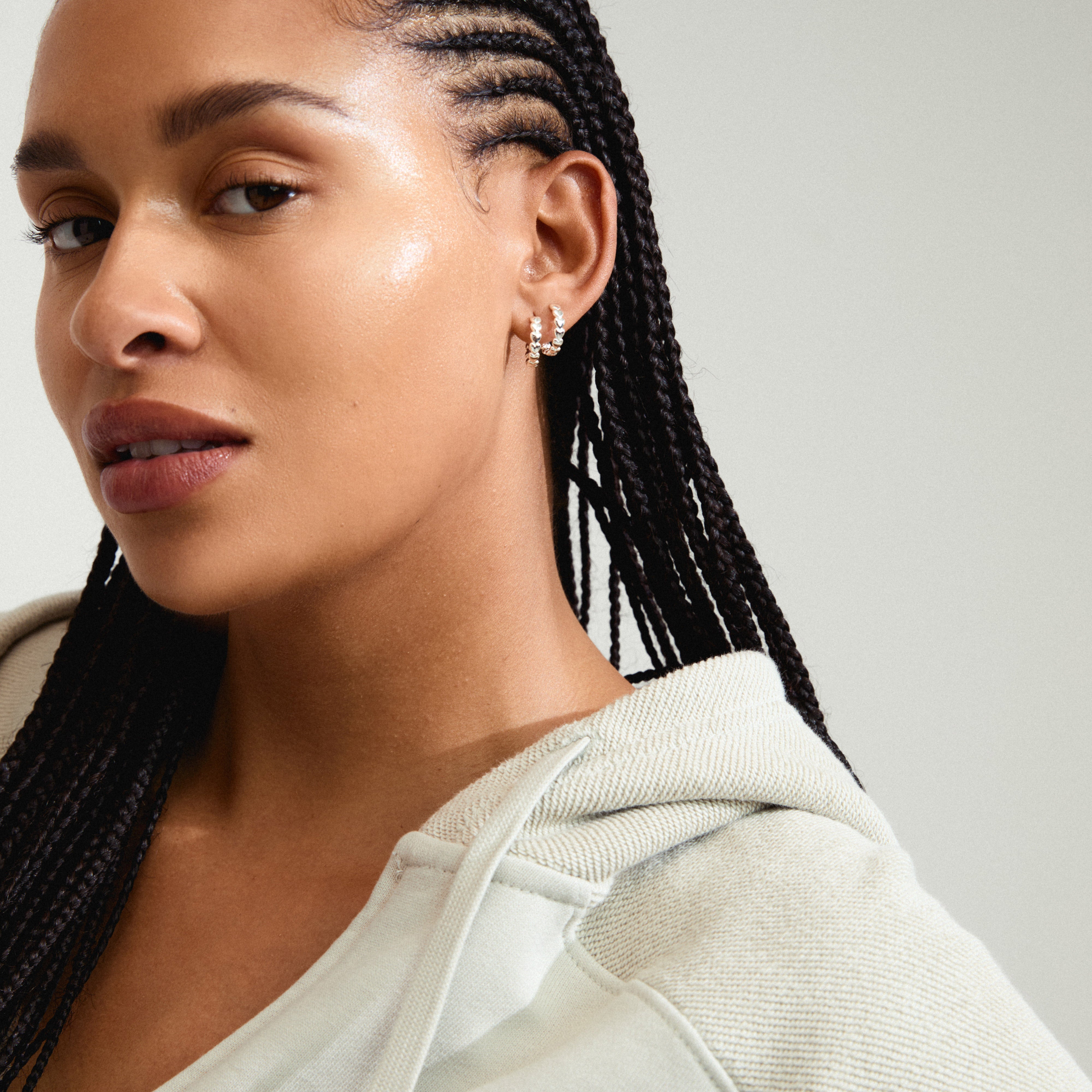 MAEVE hoop earrings silver-plated with heart pattern, worn by a woman with braided hair, showcasing stylish, eco-friendly Danish design from Pilgrim.