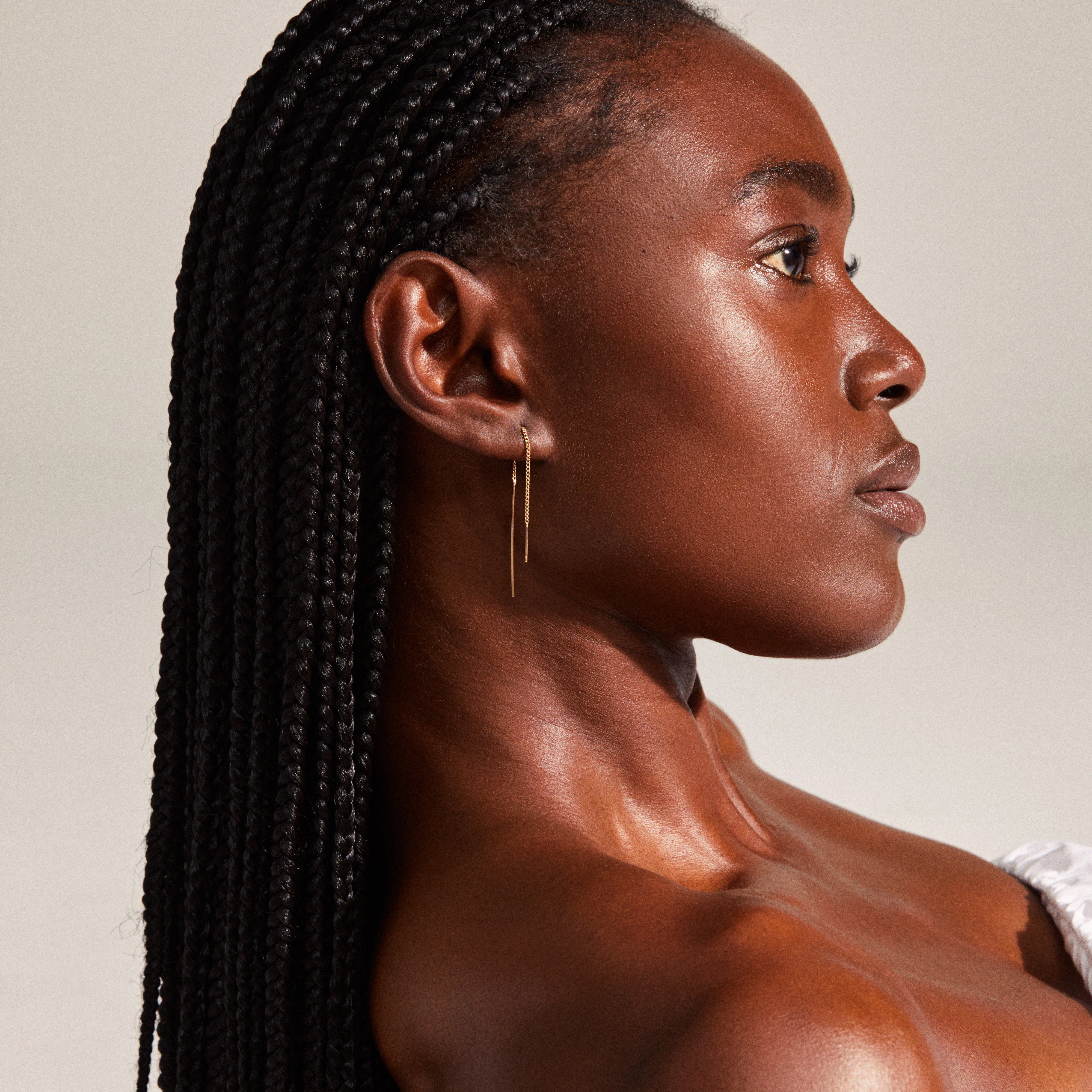 Woman with long braids wearing TAHOE chain earrings, featuring a gold-plated bar and chain design, highlighting its versatile, personalized styling potential.
