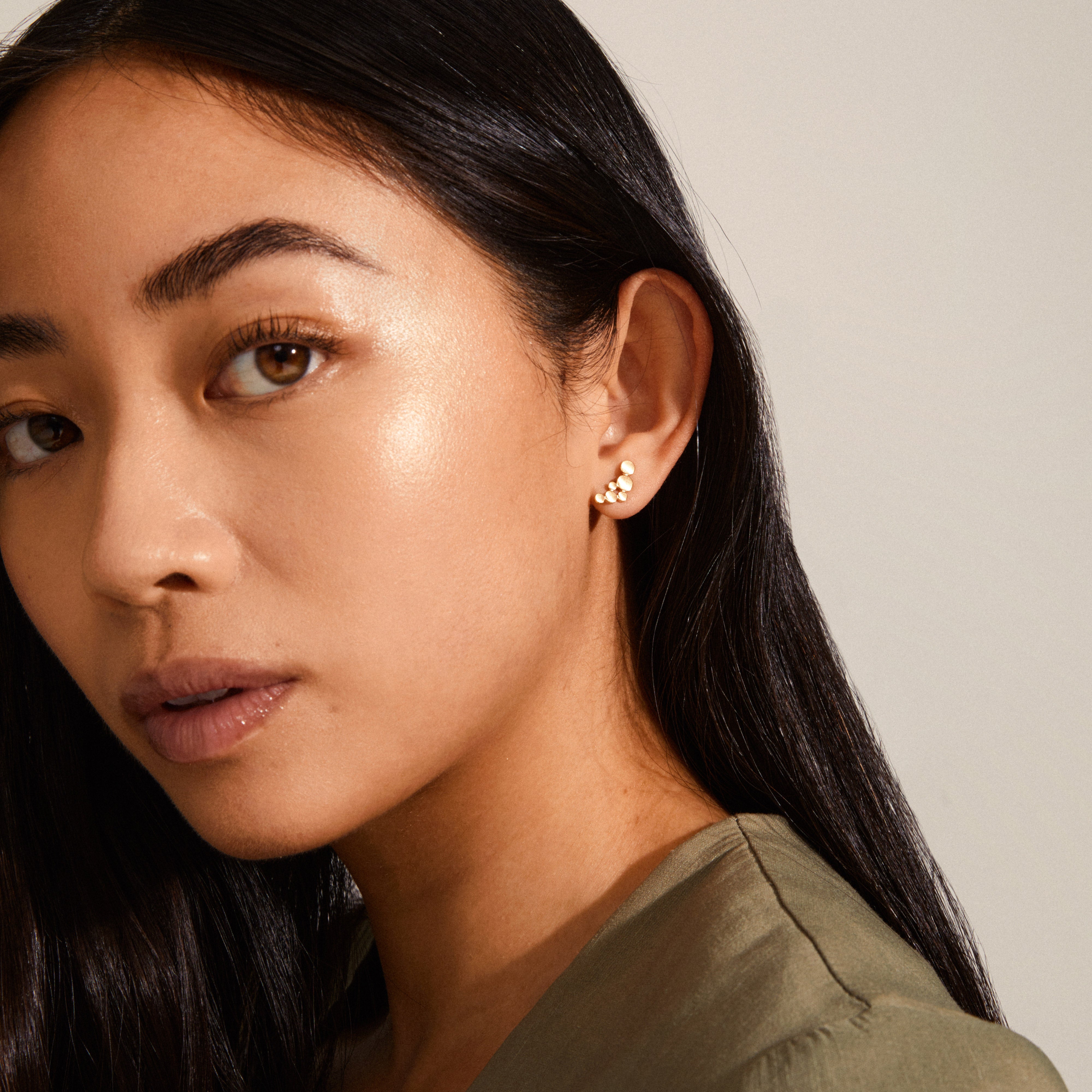 LEAH earring gold-plated: Close-up of a woman's ear showcasing elegant gold-plated studs, small circles in a harmonious pattern, satin-matte finish. Timeless design.