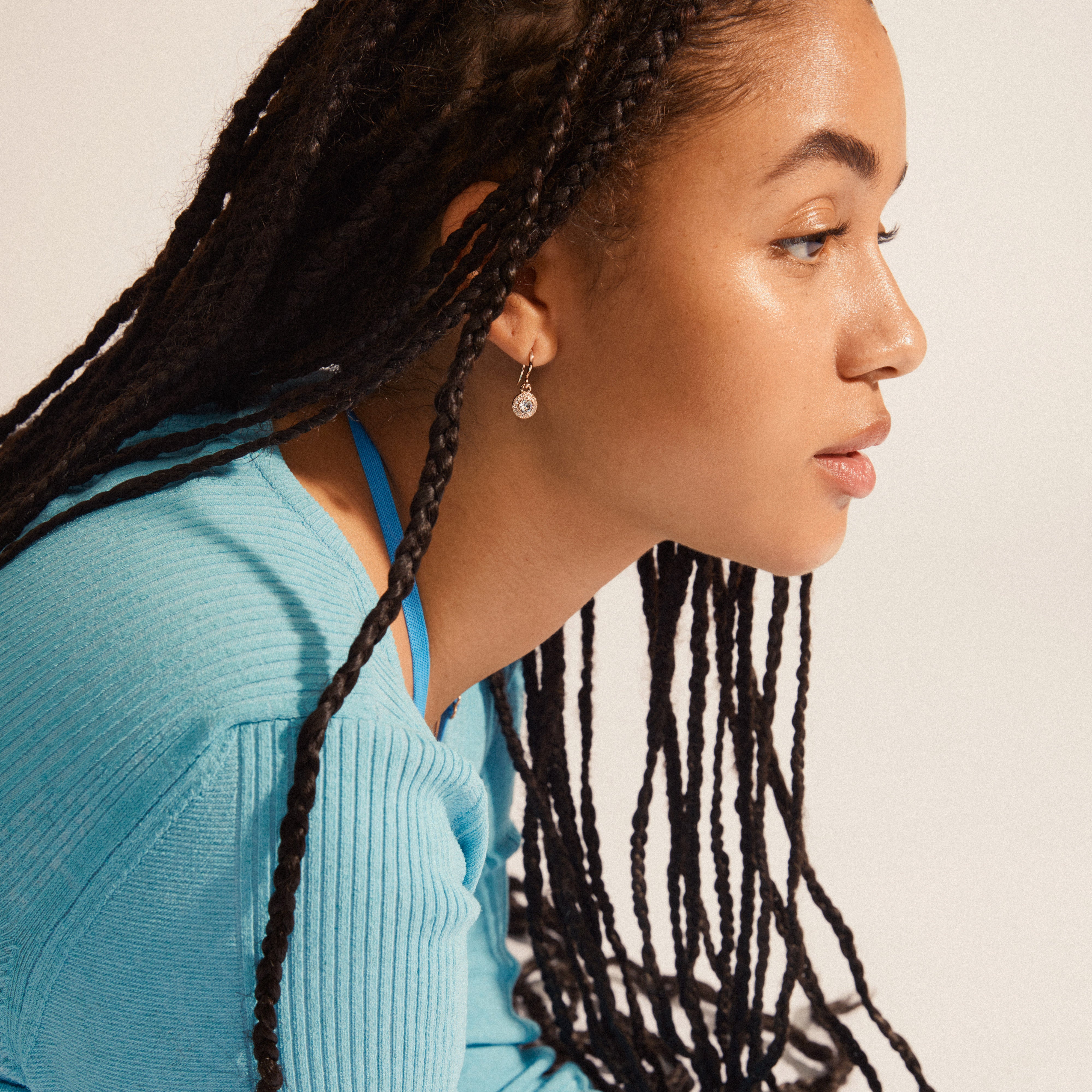 CLEMENTINE crystal earrings rosegold-plated, featuring a halo of crystals and pavé pendant, elegantly worn by a woman with braided hair.