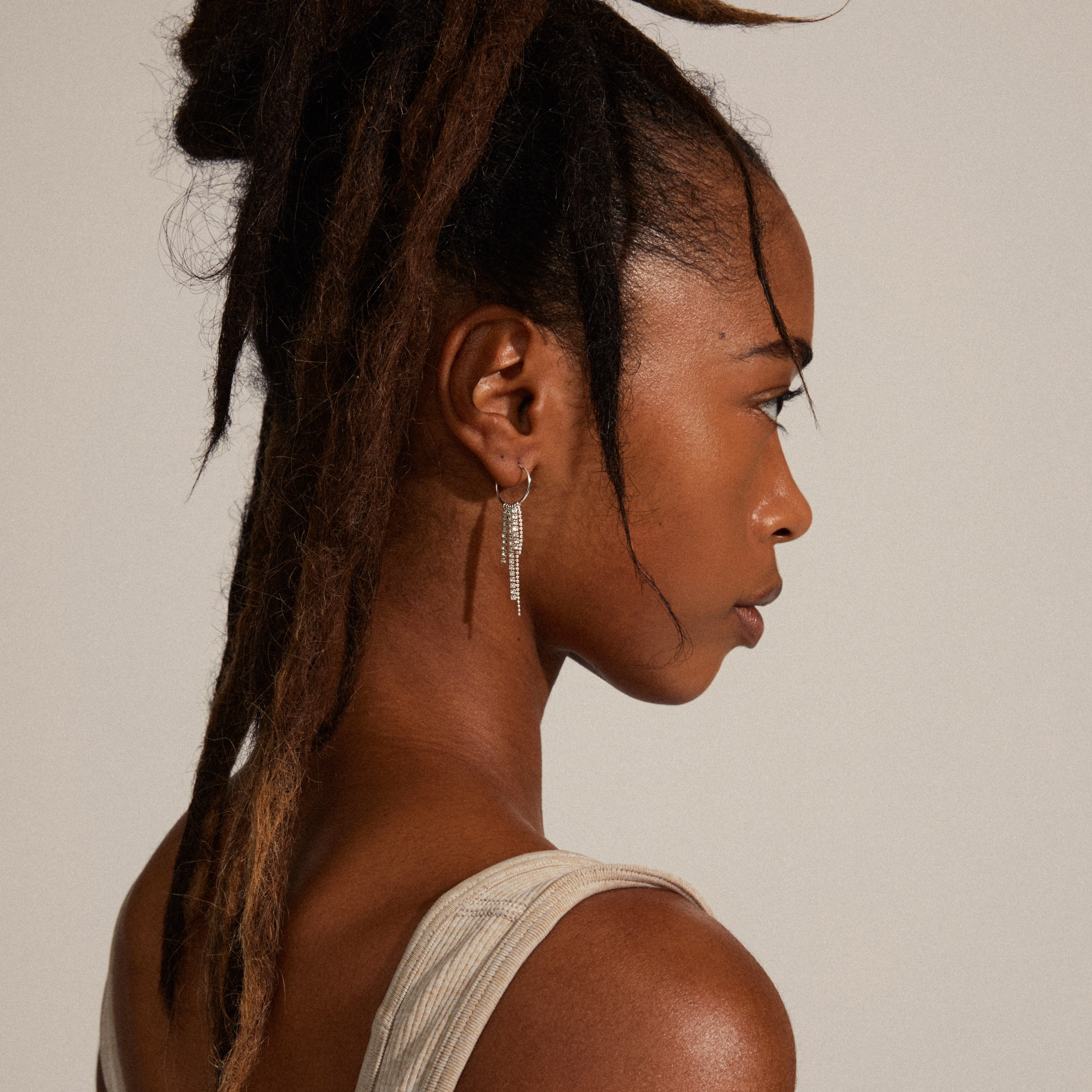 MAJA crystal waterfall hoop earrings, silver-plated, adorning a woman's ear with long hair, showcasing dangling pendants for a trendy, powerful look.