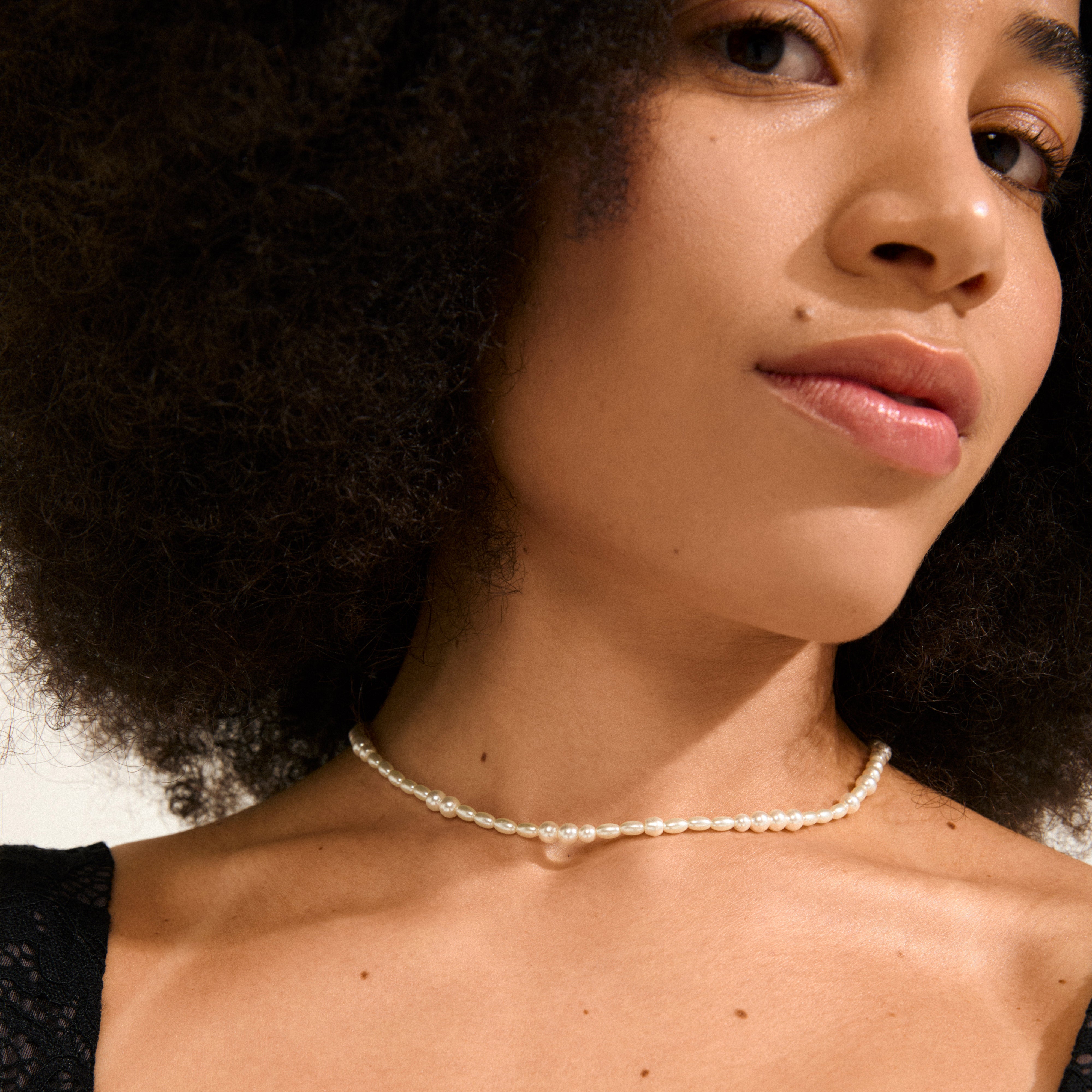 A woman wearing the ELLIANA necklace gold-plated, featuring freshwater pearls and mother-of-pearl glass beads, stylishly accentuates her elegant look.