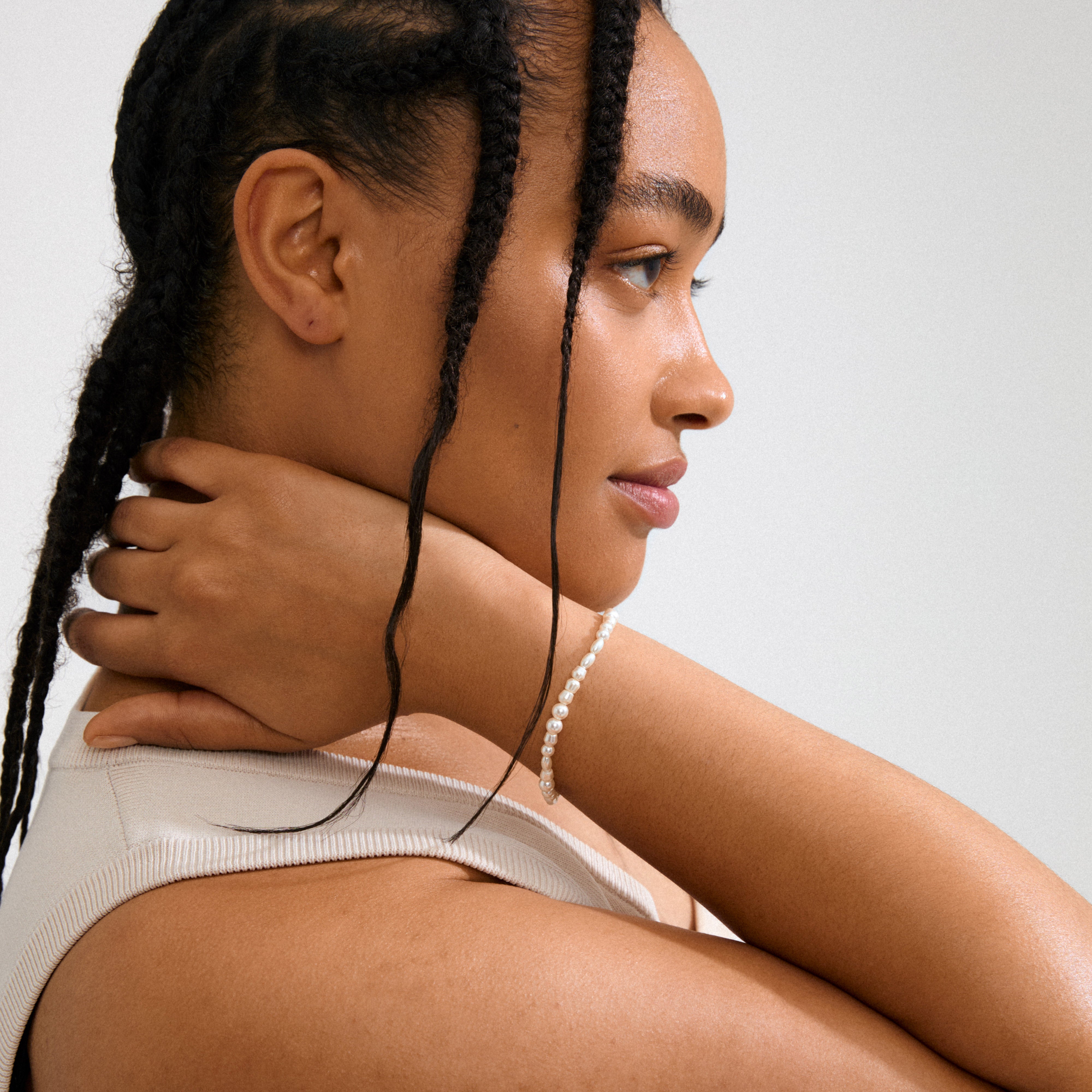 ELLIANA bracelet gold-plated, showcased on a model with braided hair, highlighting timeless freshwater pearls and mother-of-pearl glass beads for elegant style.