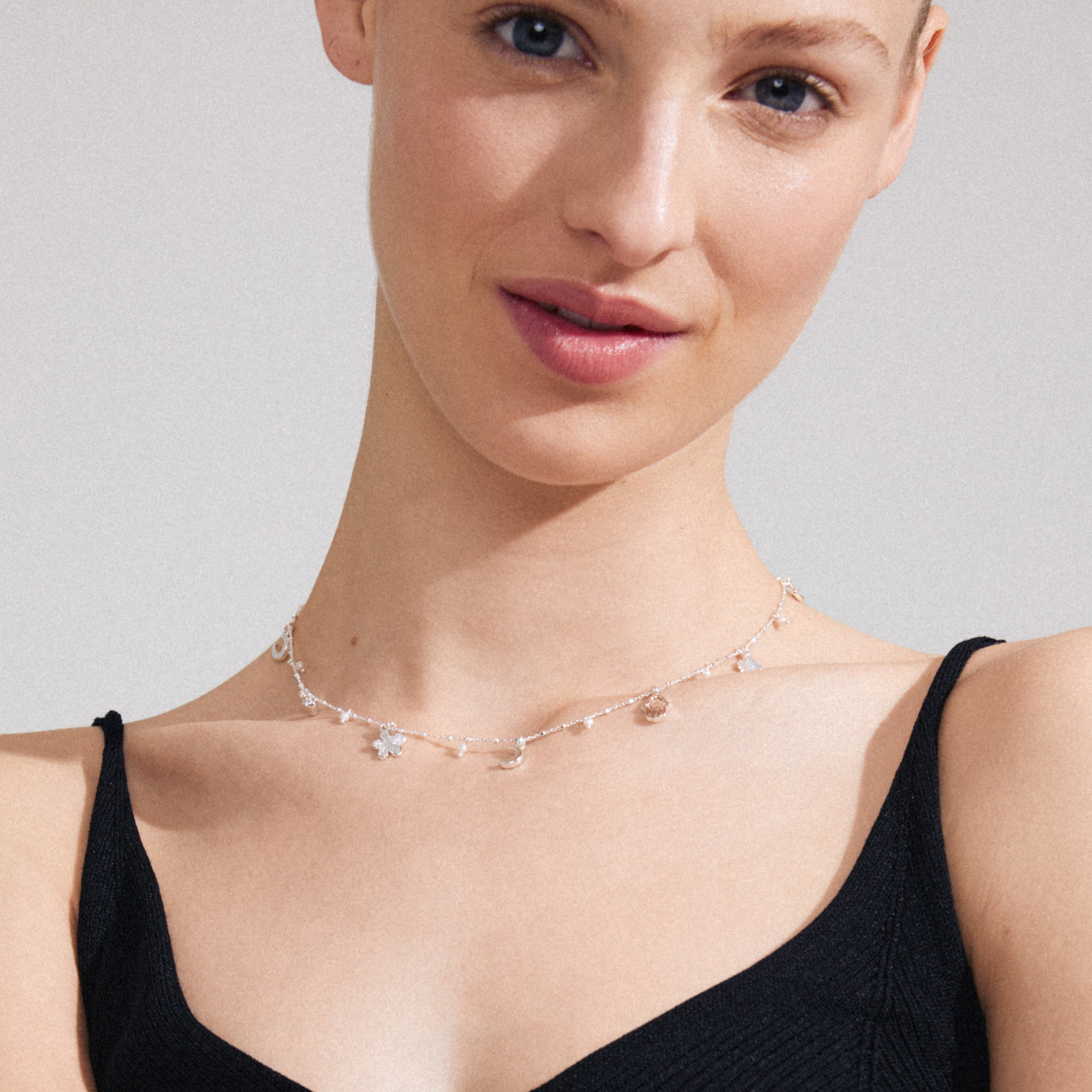 PRUCENCE necklace silver-plated on woman's neck, featuring charms like hearts and moons, with freshwater pearls and Preciosa crystals, symbolizing elegance and storytelling.
