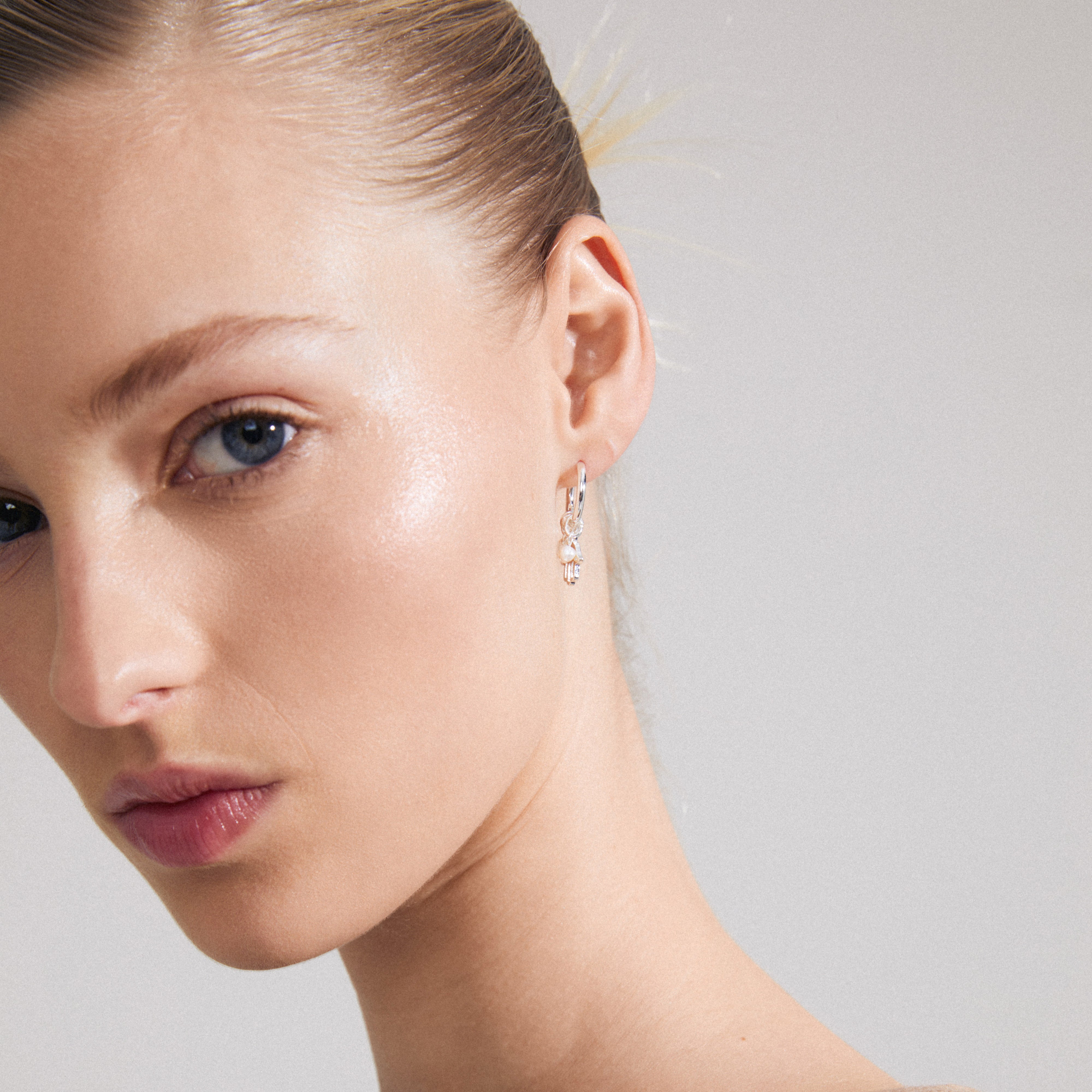 Close-up of a woman's ear wearing Pilgrim's PRUCENCE silver-plated earrings, featuring tiny charms, freshwater pearl, and Preciosa crystals.