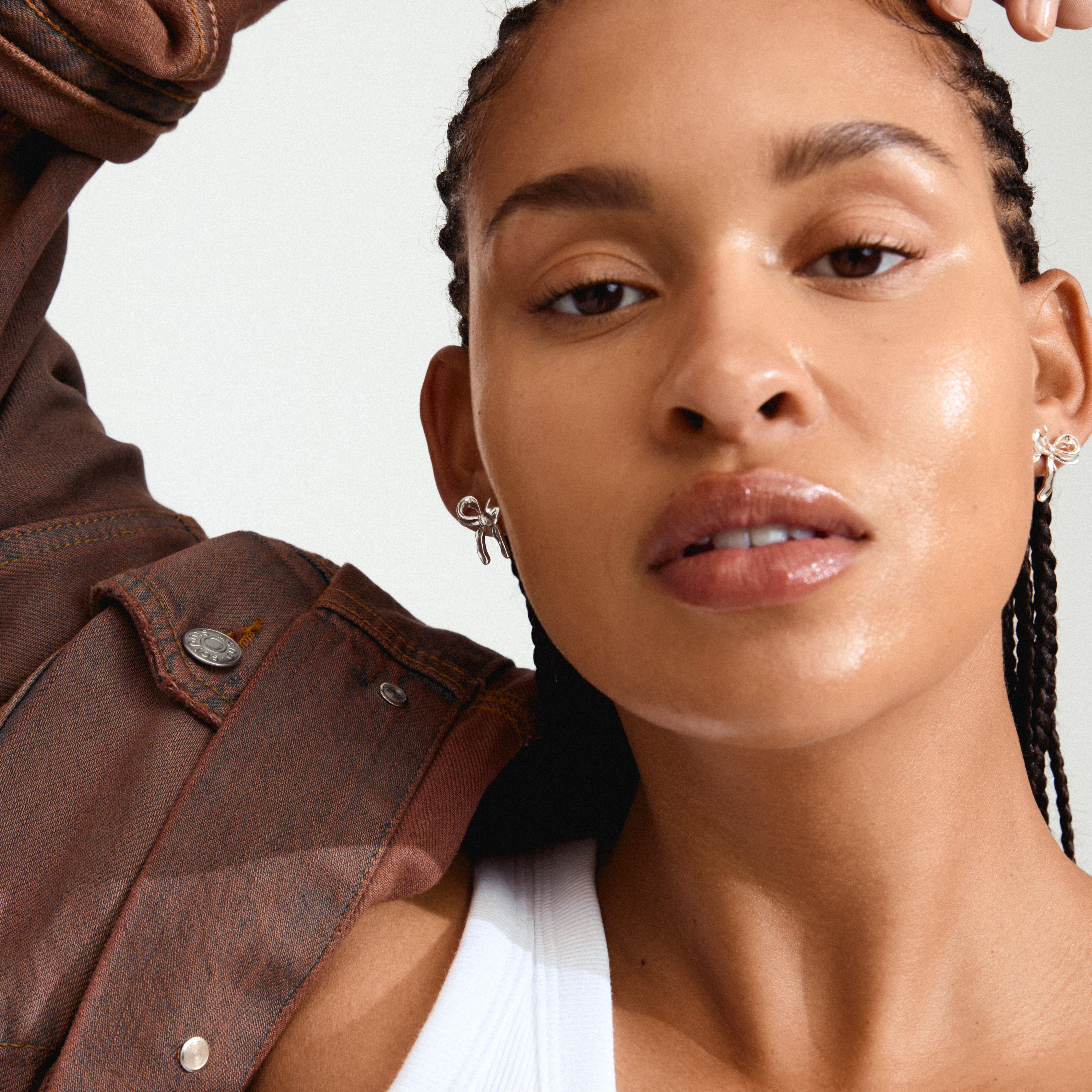CASSIAN earrings silver-plated: A woman with braids wears silver bow earrings, highlighting their trendy and timeless design suitable for this season's fashion.