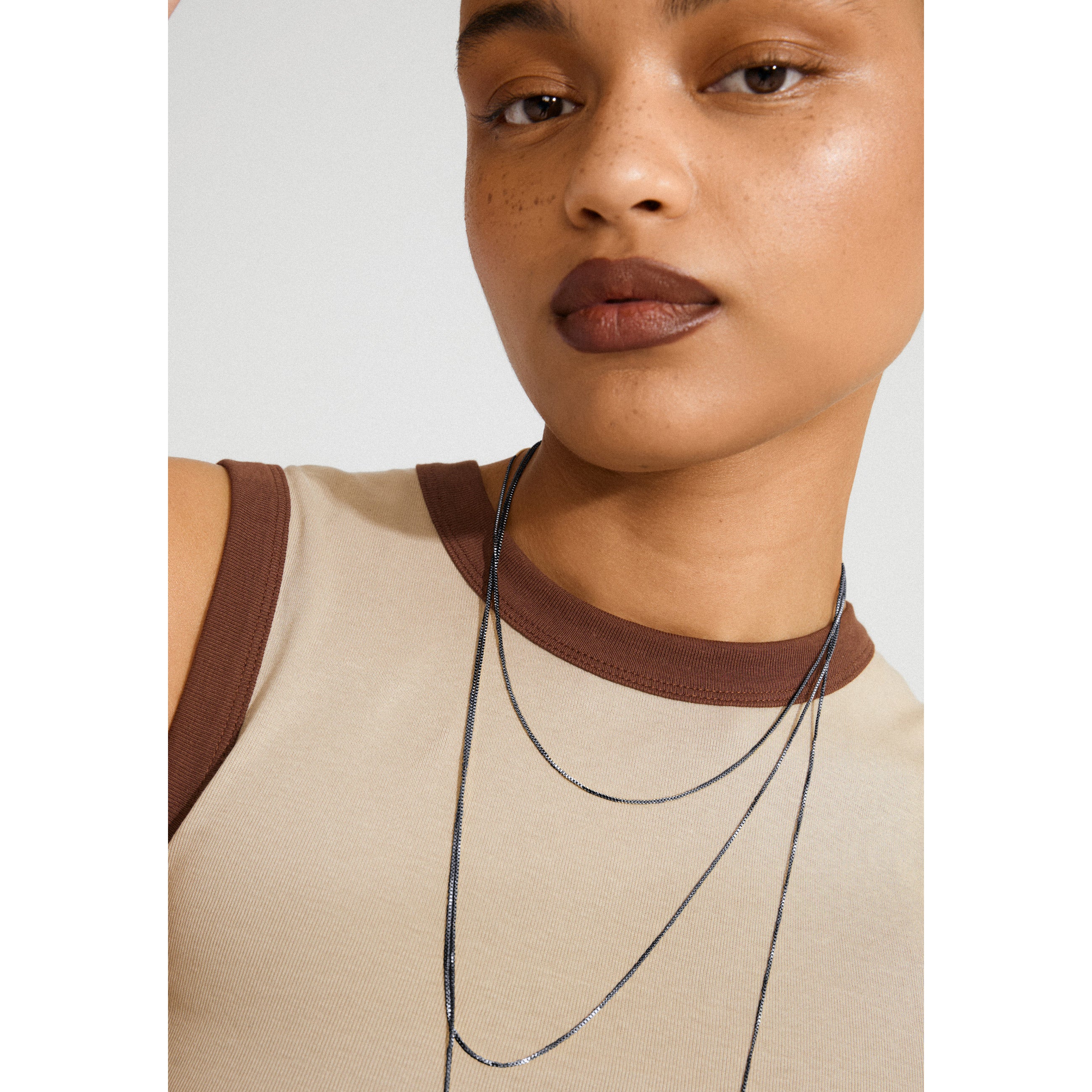 Close-up of a human face wearing the NANCY necklace, a 60 cm hematite-plated Venezia chain, highlighting its simplicity and versatility for layering or adding pendants.