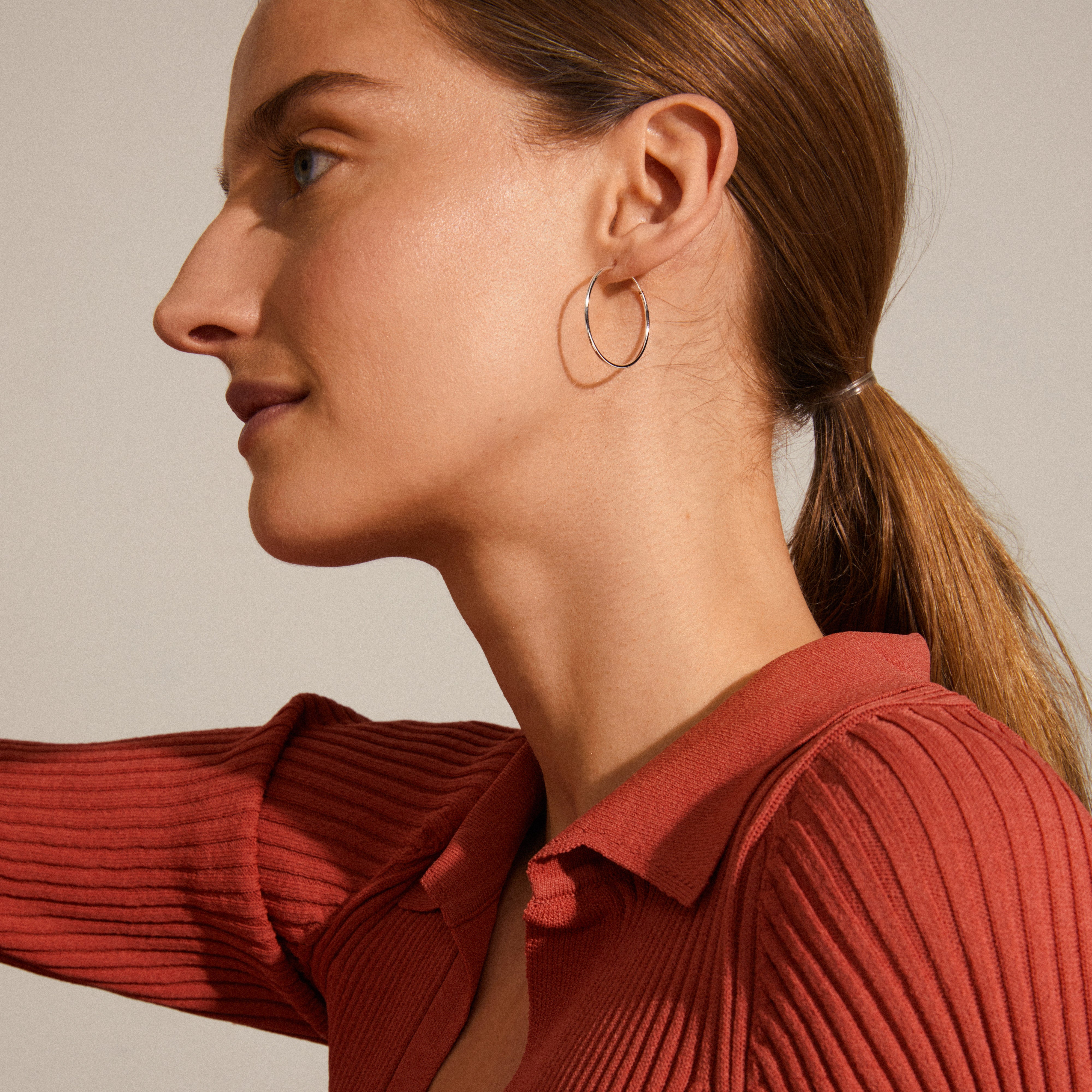 SANNE medium hoop earrings, silver-plated, showcased on a woman. These 26 mm hoops offer timeless elegance and versatility for everyday wear or personalized styling.