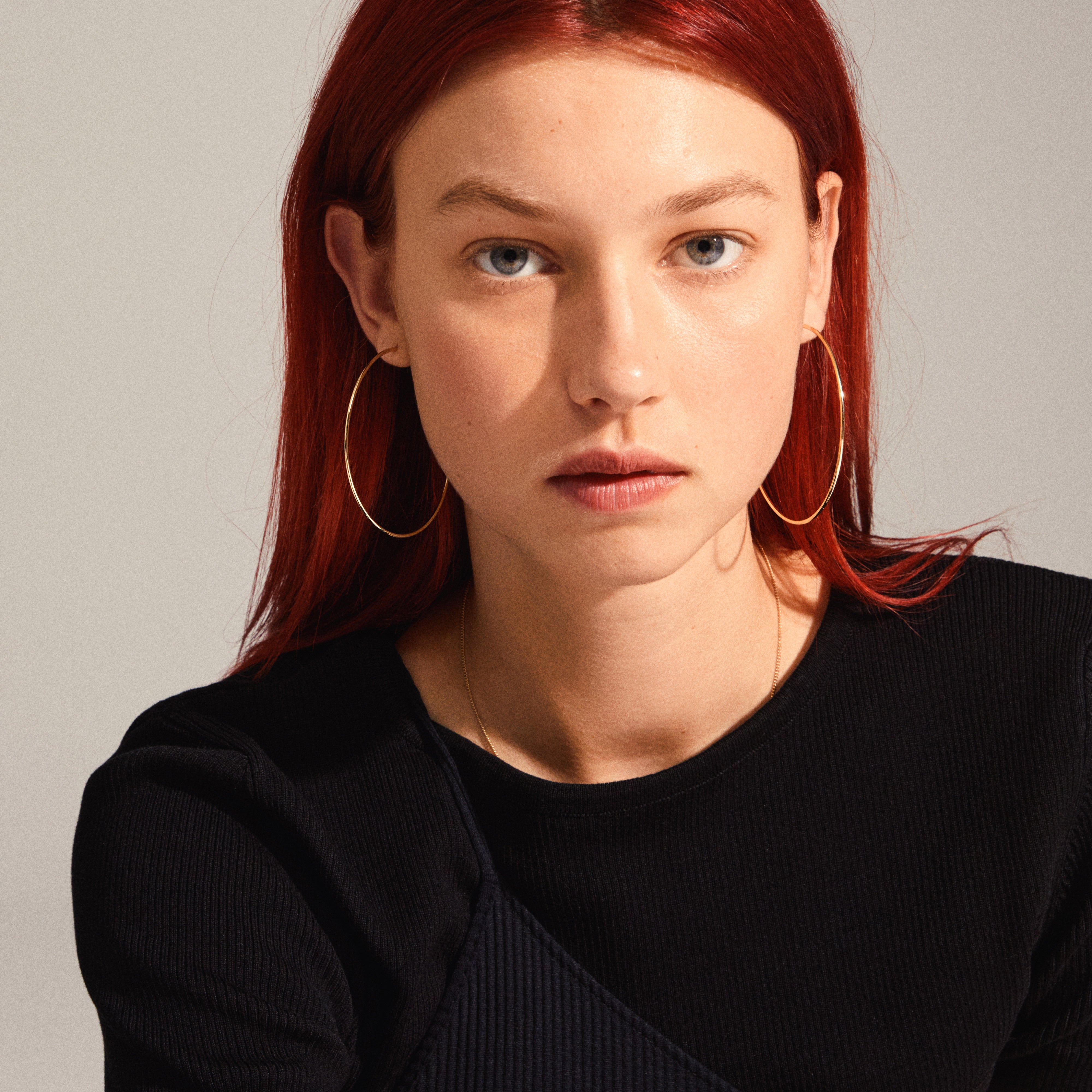 Woman with red hair wearing Pilgrim's SANNE X-large gold-plated hoop earrings, showcasing their sleek, airy design and 60 mm size.