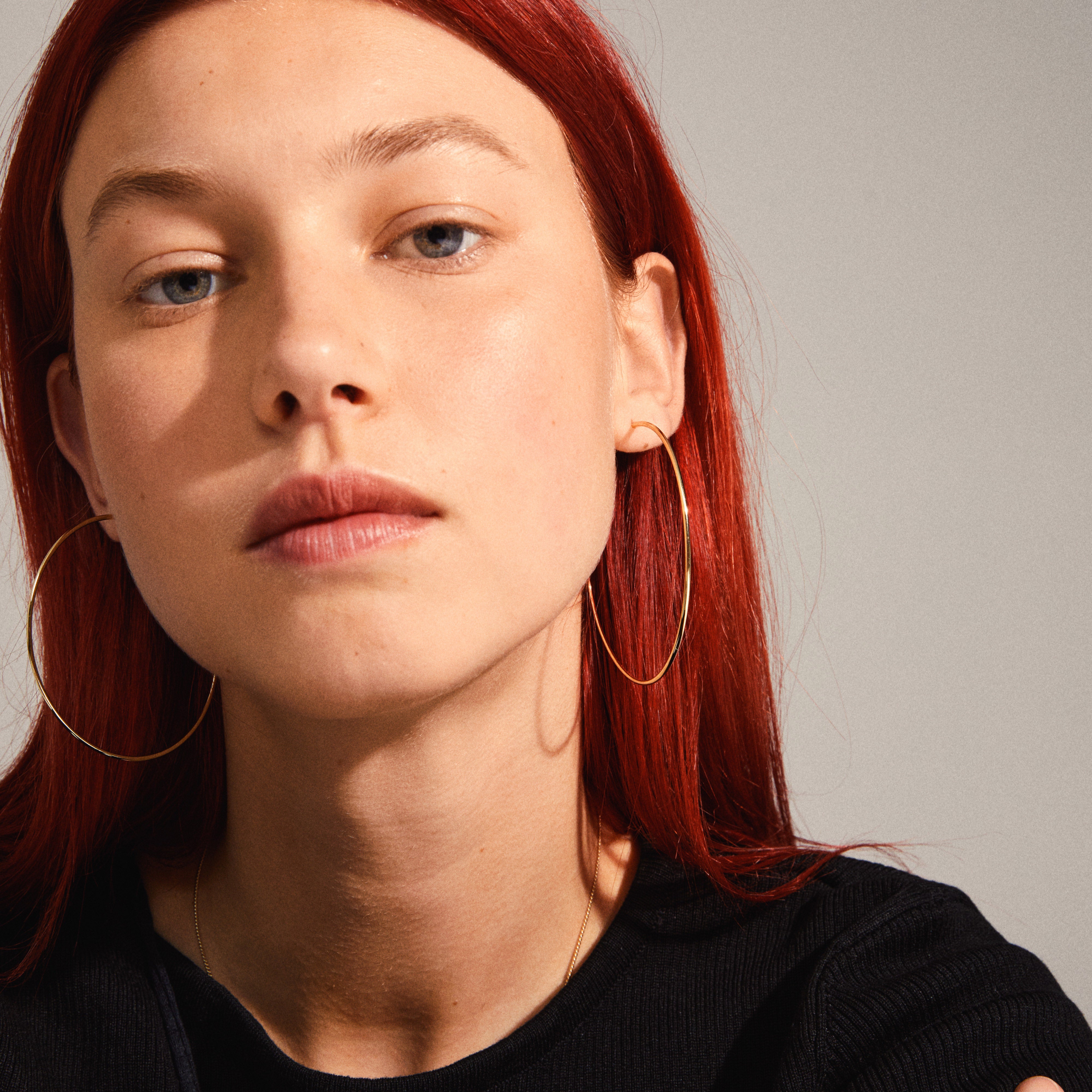 SANNE X-large gold-plated hoop earrings showcased on a red-haired woman, highlighting the earrings' sleek, airy design and large 60 mm size.