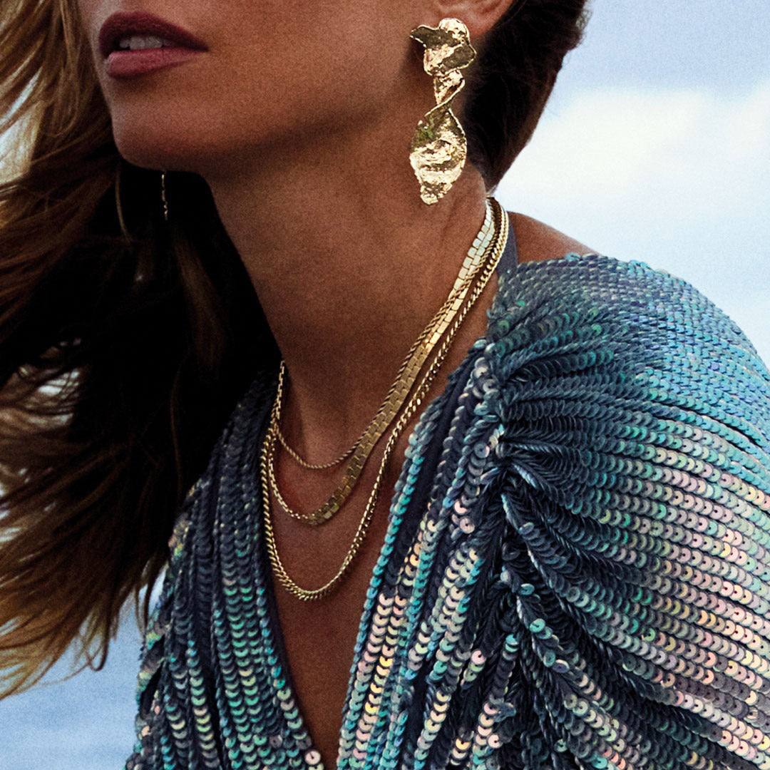 Woman wearing the gold-plated PAM robe chain necklace, featuring a chunky, twisted cord design, elegantly styled with gold earrings and a blue dress.