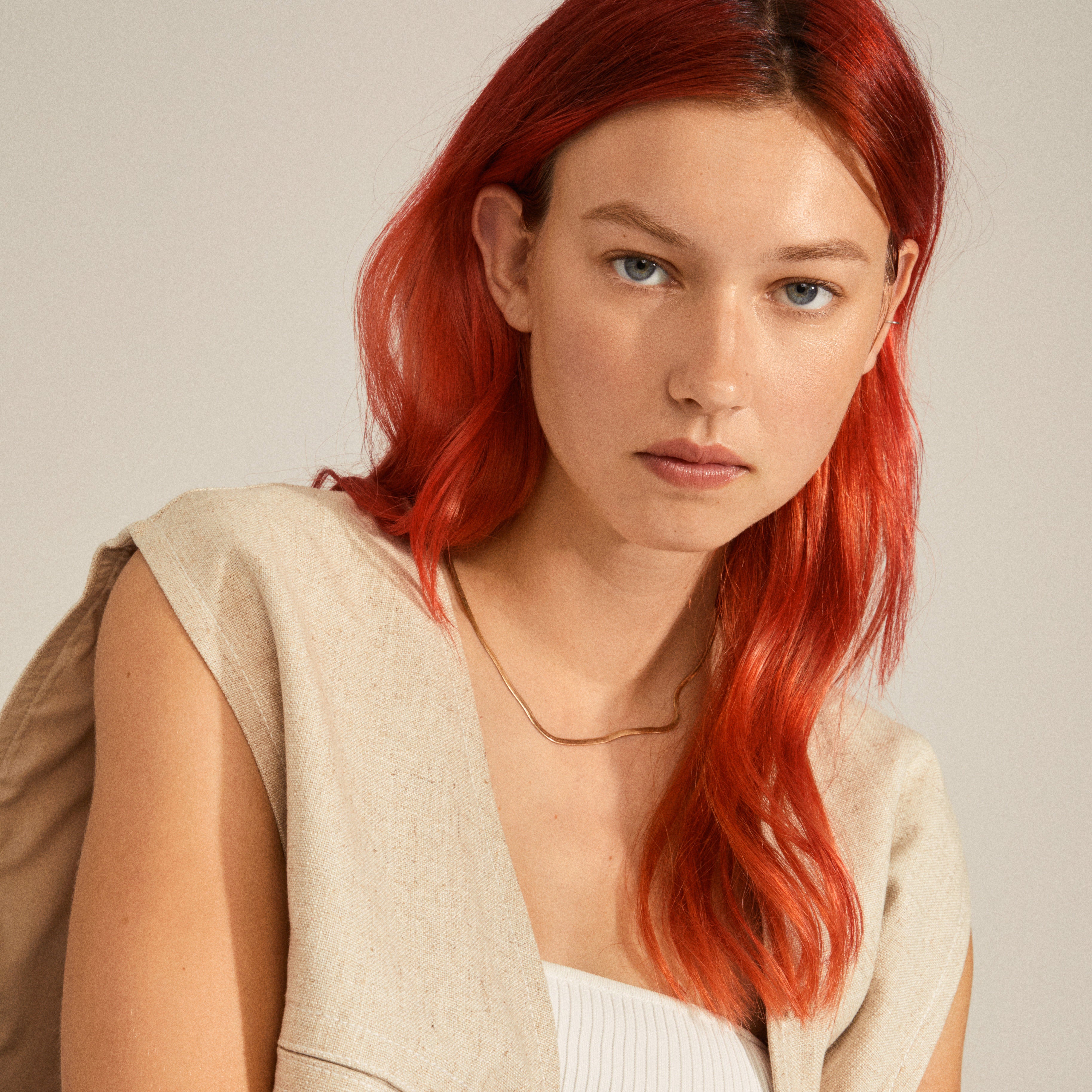 A woman with red hair wears the JOANNA flat snake chain necklace, gold-plated, highlighting its timeless elegance and Scandinavian craftsmanship from Pilgrim's Classics collection.