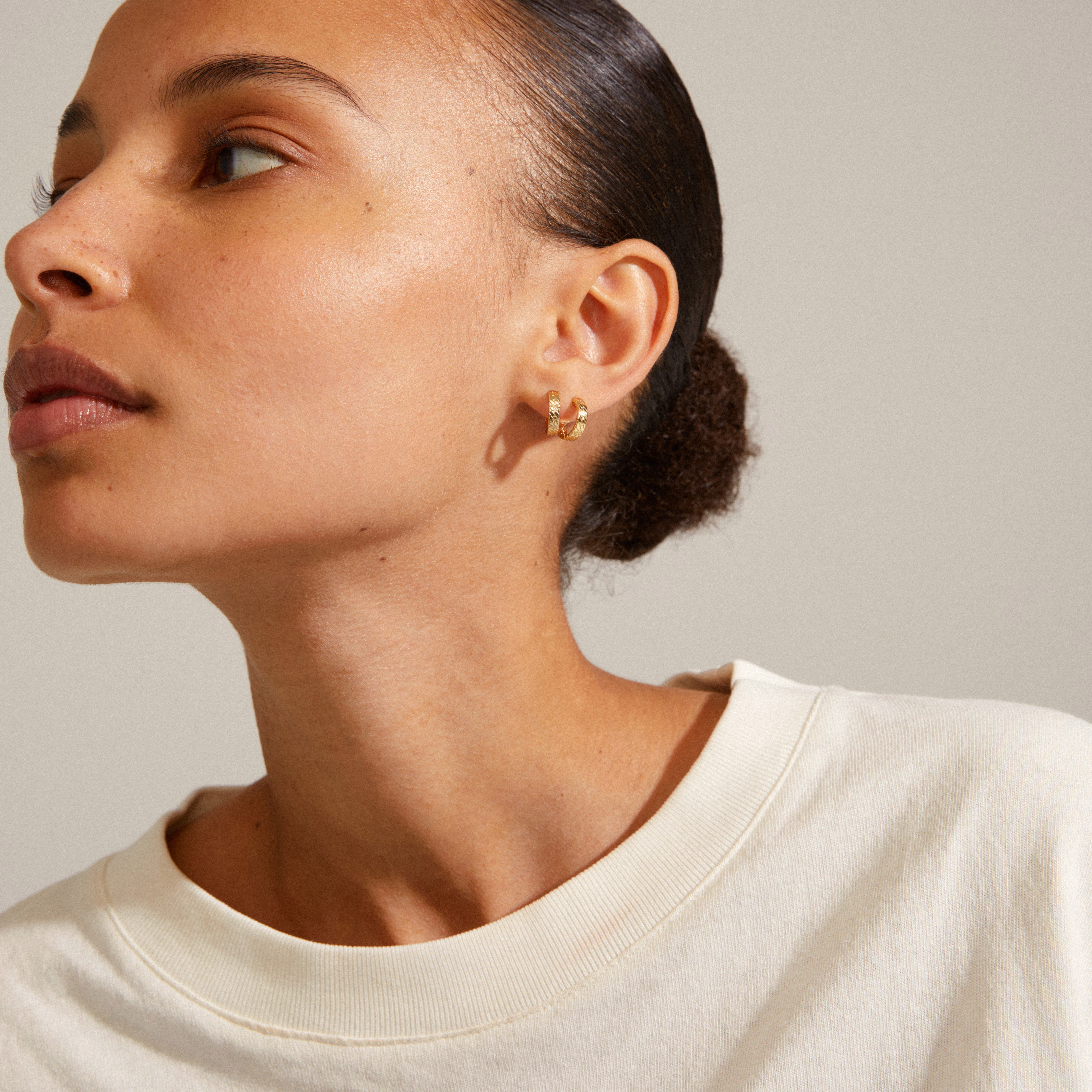 Close-up of a woman wearing JOANNA snake chain gold-plated hoop earrings from Pilgrim, showcasing the raw chain structure inspired by a Nordic style.