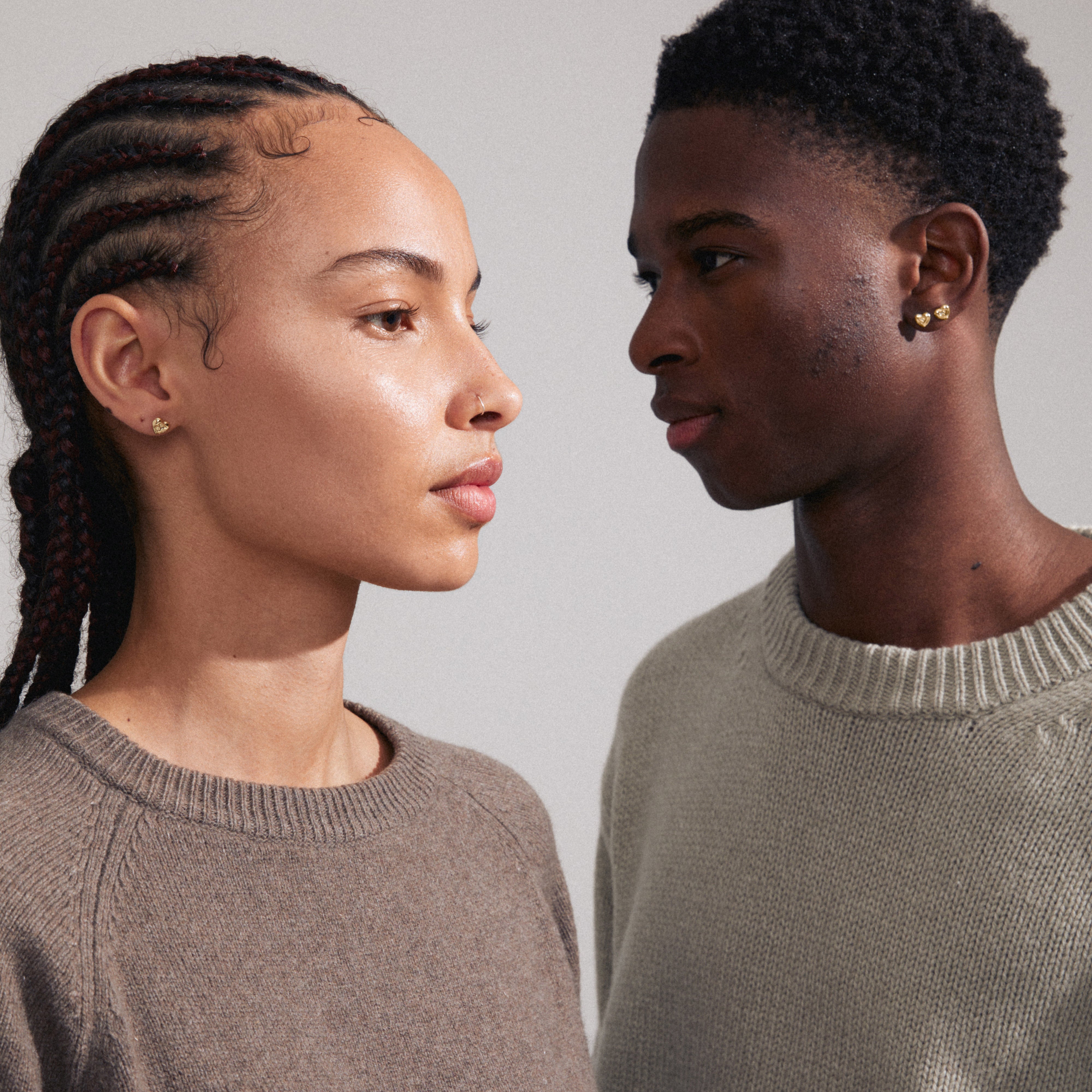 A man and woman wear the ARLET gold-plated heart stud earrings, showcasing the timeless Pilgrim design made from recycled materials.