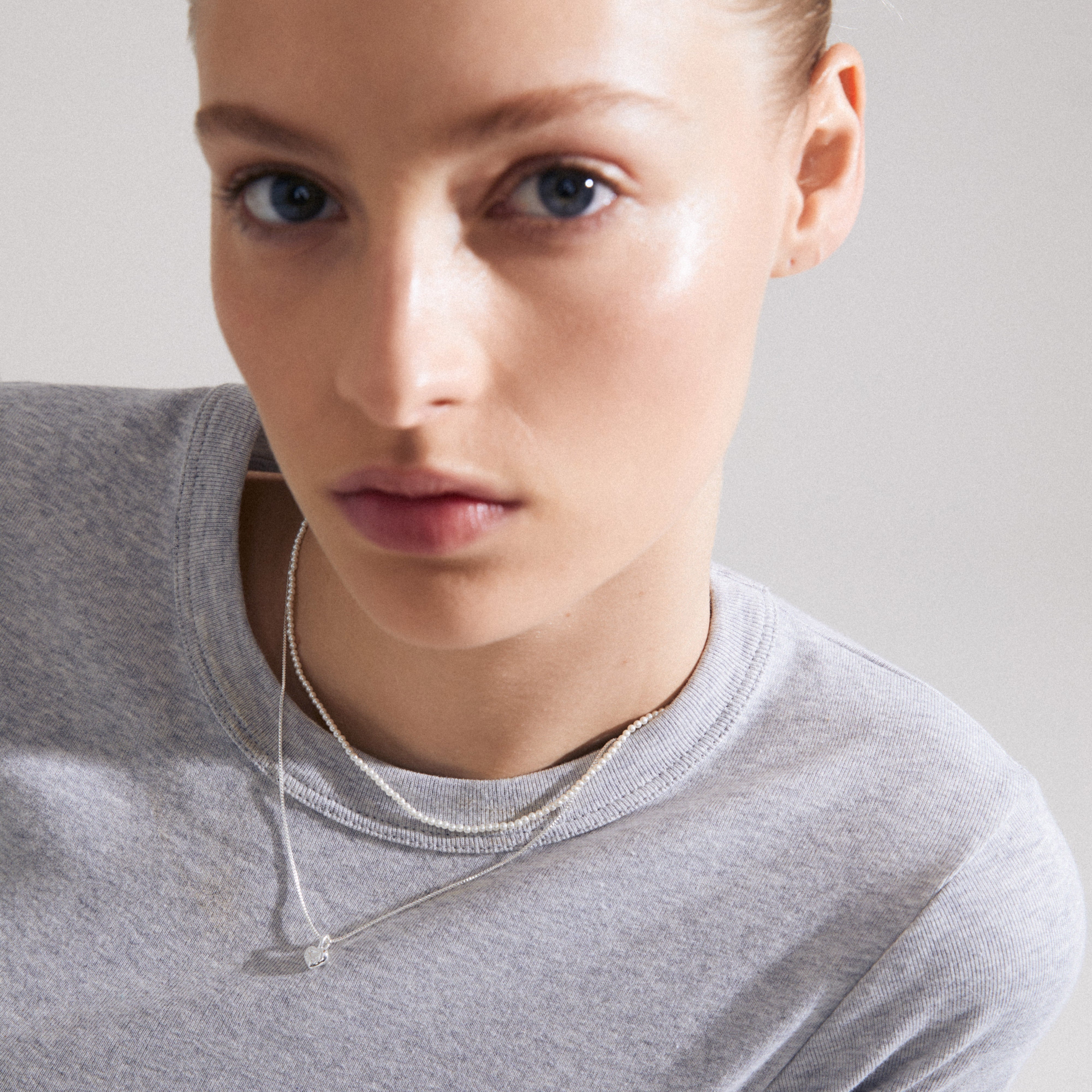 Close-up of a woman wearing Pilgrim's ARLET necklace 2-in-1 set, featuring a silver-plated chain with a heart pendant and a pearl necklace.
