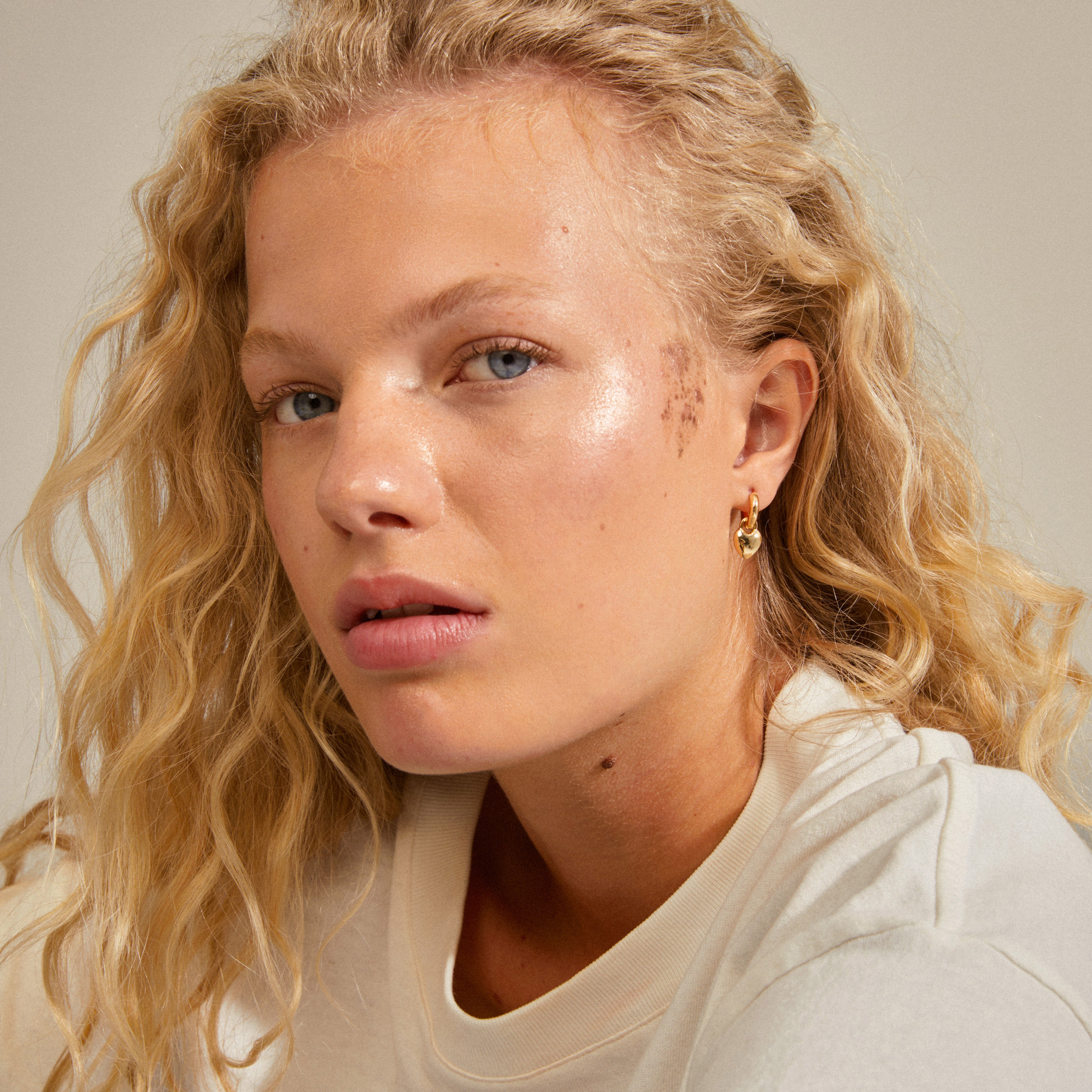 SOPHIA heart hoops gold-plated adorn a woman's ear, showcasing their elegant heart pendants. These versatile earrings highlight her face subtly and stylishly.