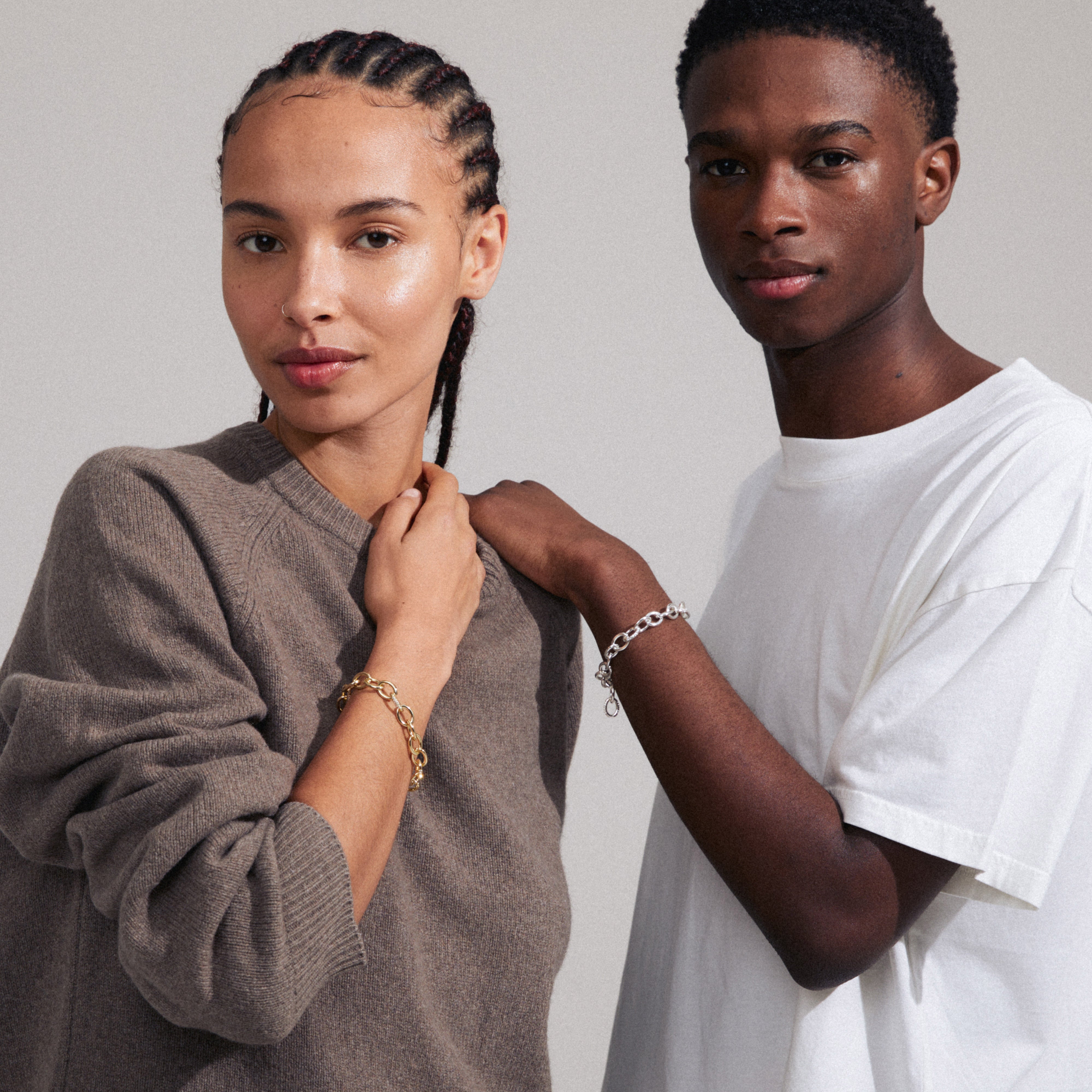 AMIRI gold-plated bracelet with sparkling Preciosa crystals, showcasing a fluid cable chain design, worn by a woman with braids in a brown sweater.