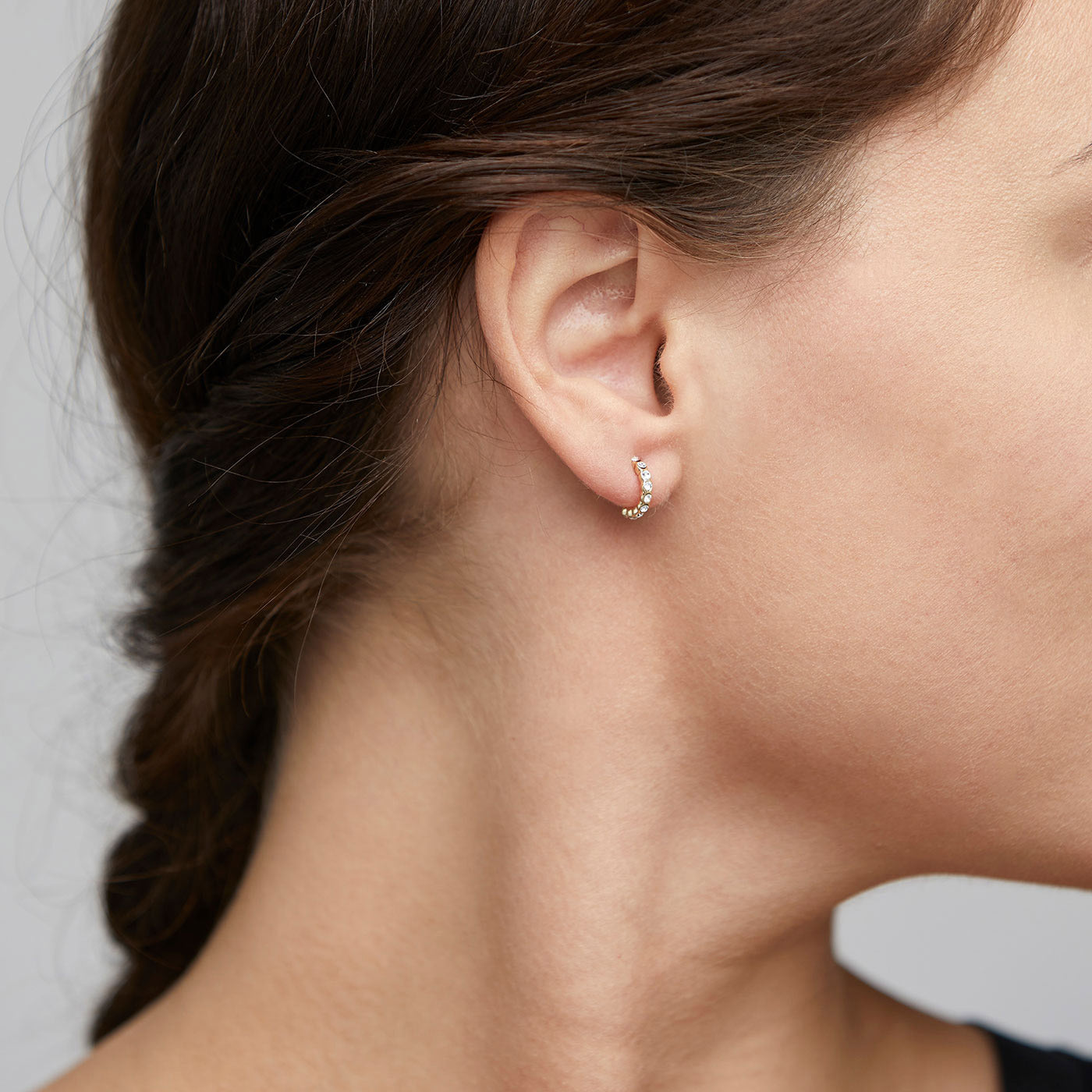 BRIGITTE crystal half hoops gold-plated adorn a woman's ear, featuring sparkling round crystals and an elegant, undulating edge that enhances light reflections.