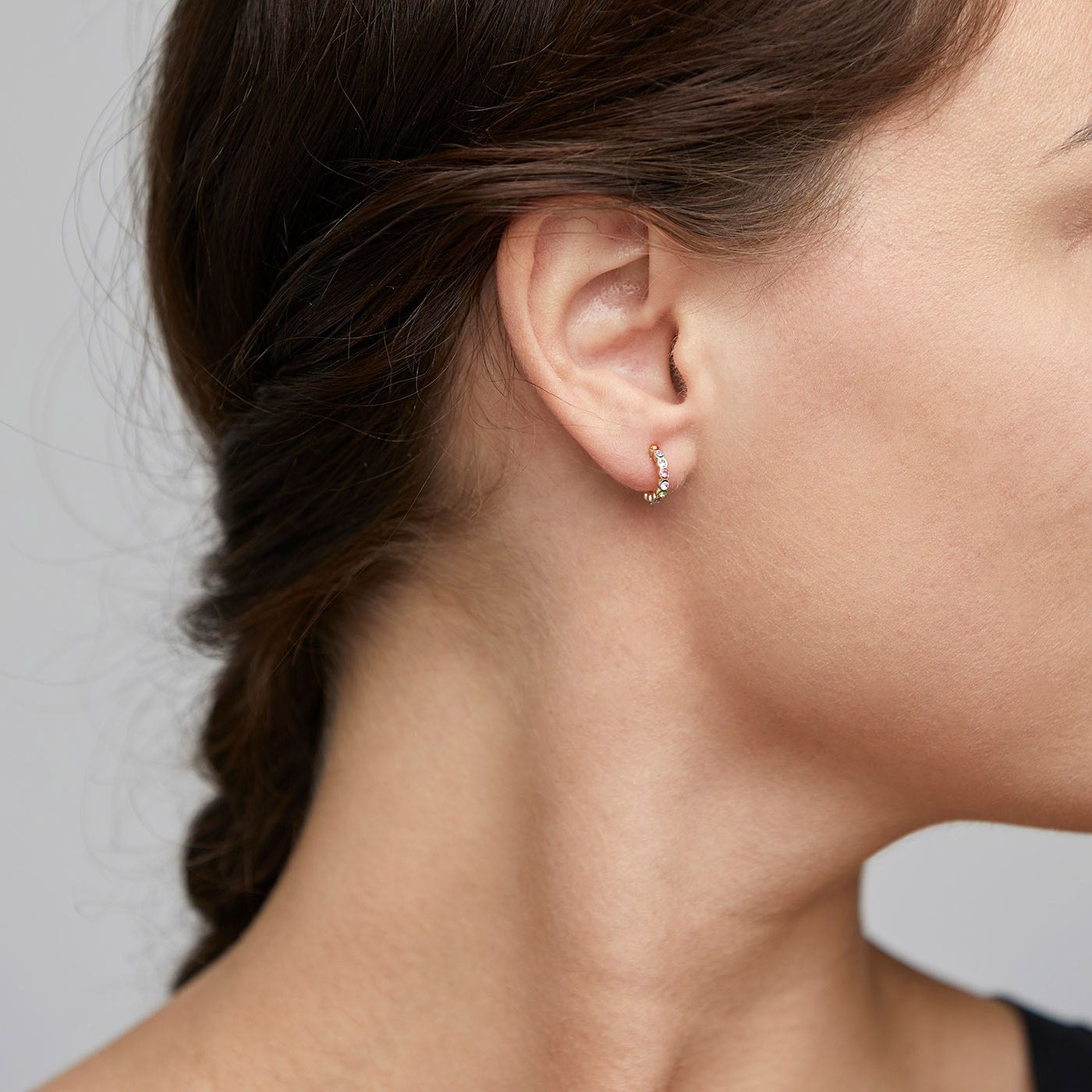 Close-up of a woman's ear wearing BRIGITTE multicolored crystal half hoops, gold-plated, showcasing elegant, sparkling design and luxurious reflections.