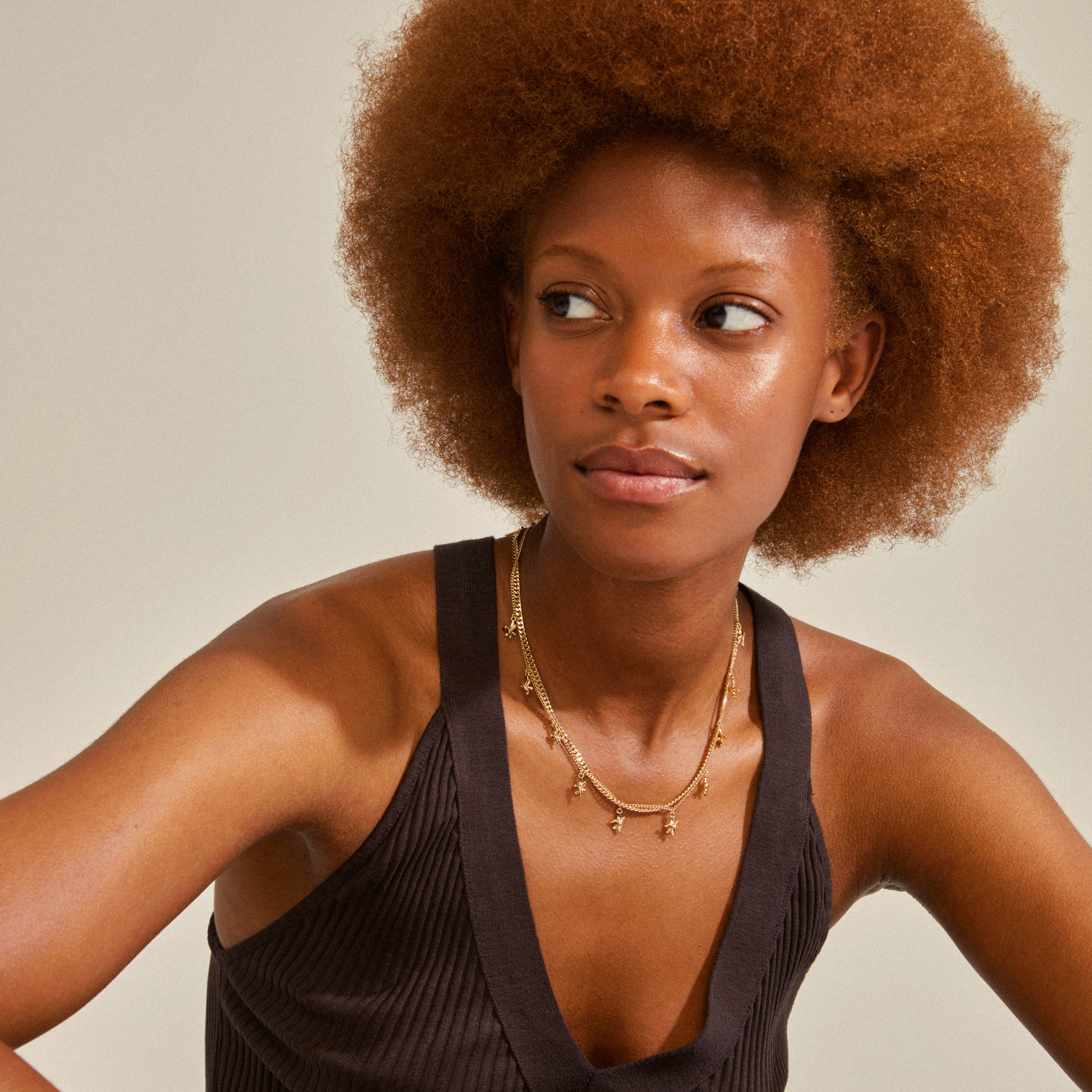 RIKO necklaces, 2-in-1 set, gold-plated, featuring a woman with curly hair wearing the layered chains; one with flower pendants, another a slim curb chain.