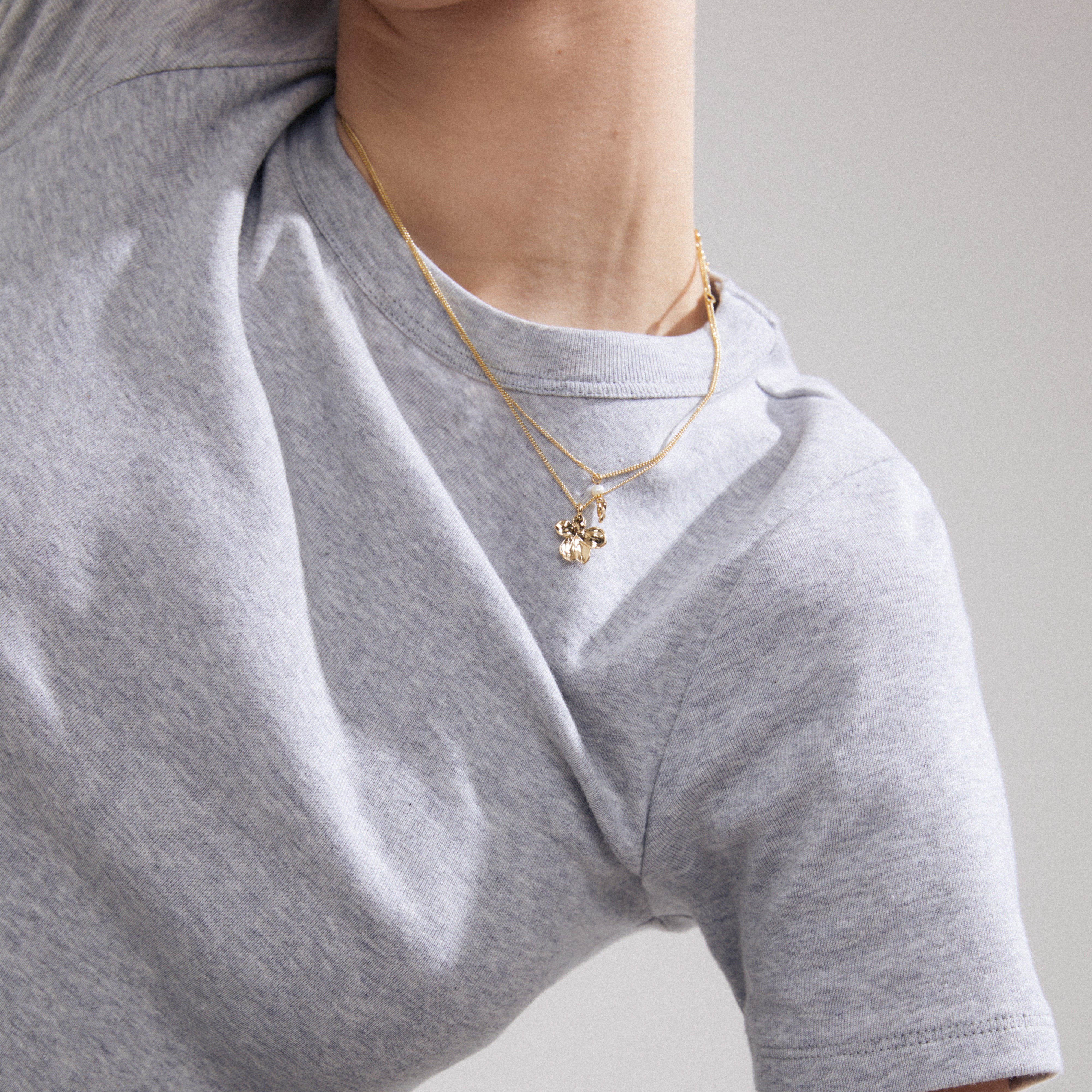 ZHURI 2-in-1 gold-plated necklace set featuring a floral pendant and pearl accents, worn by a person, highlighting its layered style and romantic design.