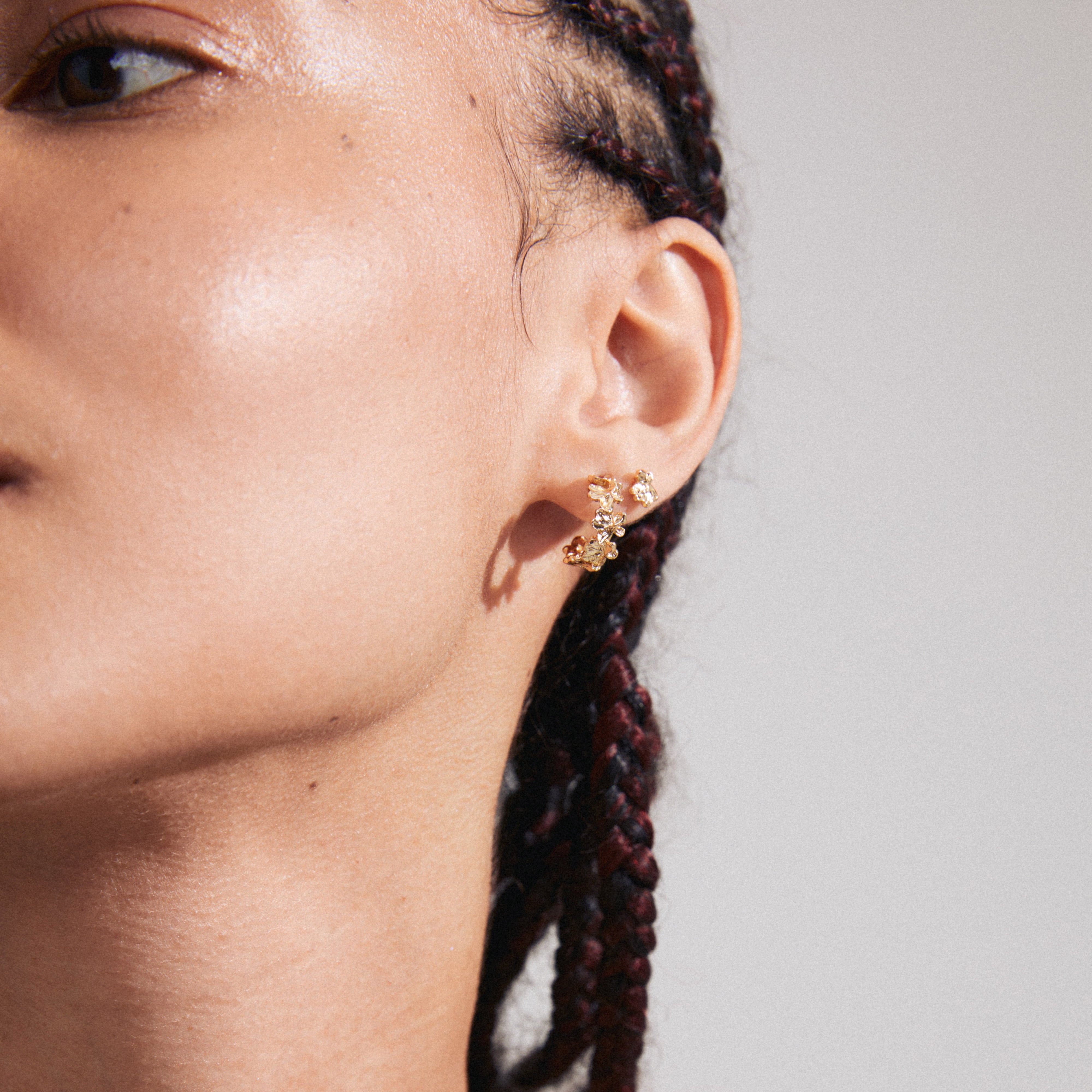 Close-up of a woman's ear adorned with the ZHURI earrings 2-in-1 set, featuring gold-plated floral half-hoops and studs by Pilgrim.
