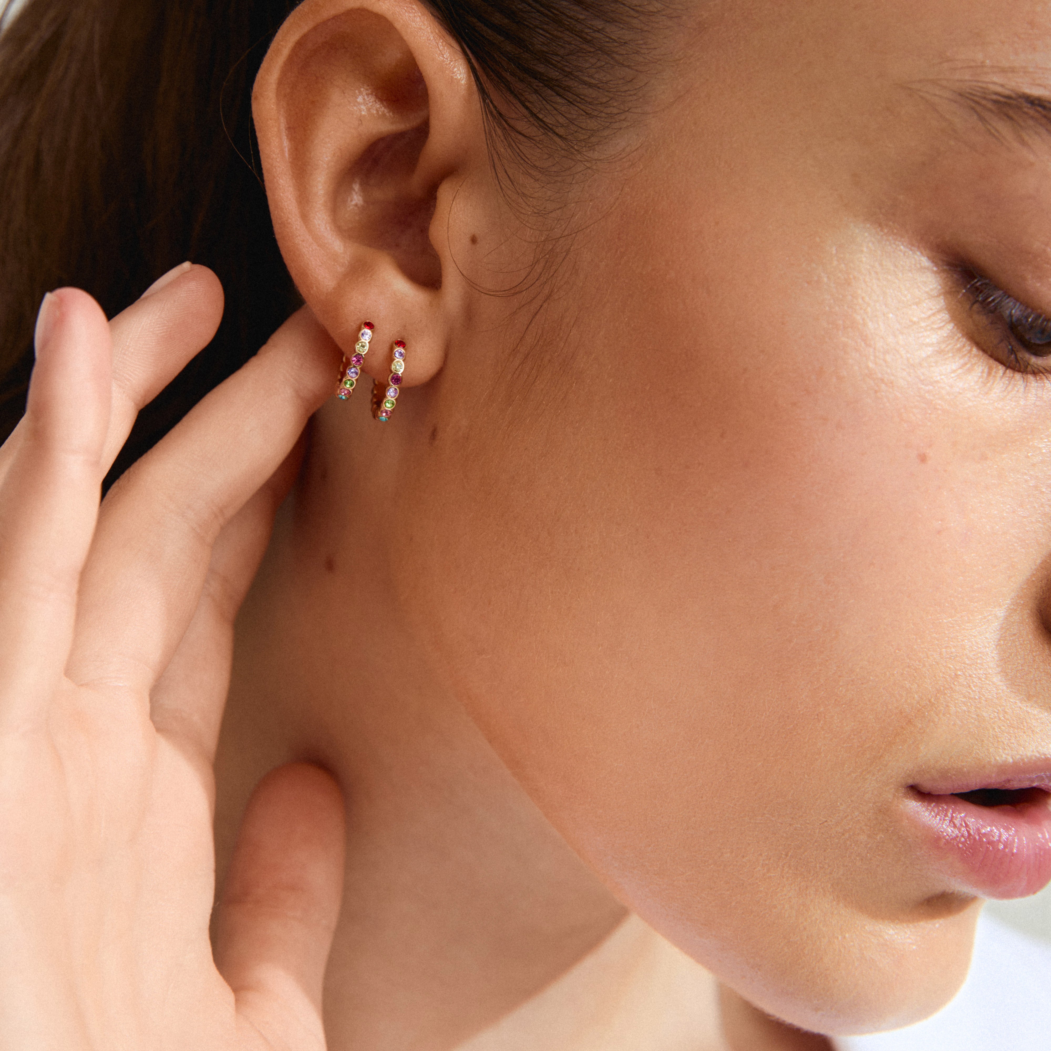 KLEOPRATRA gold-plated hoop earrings with colorful Preciosa crystals on a woman's ear, showcasing their sparkle and easy-to-use click clasp.