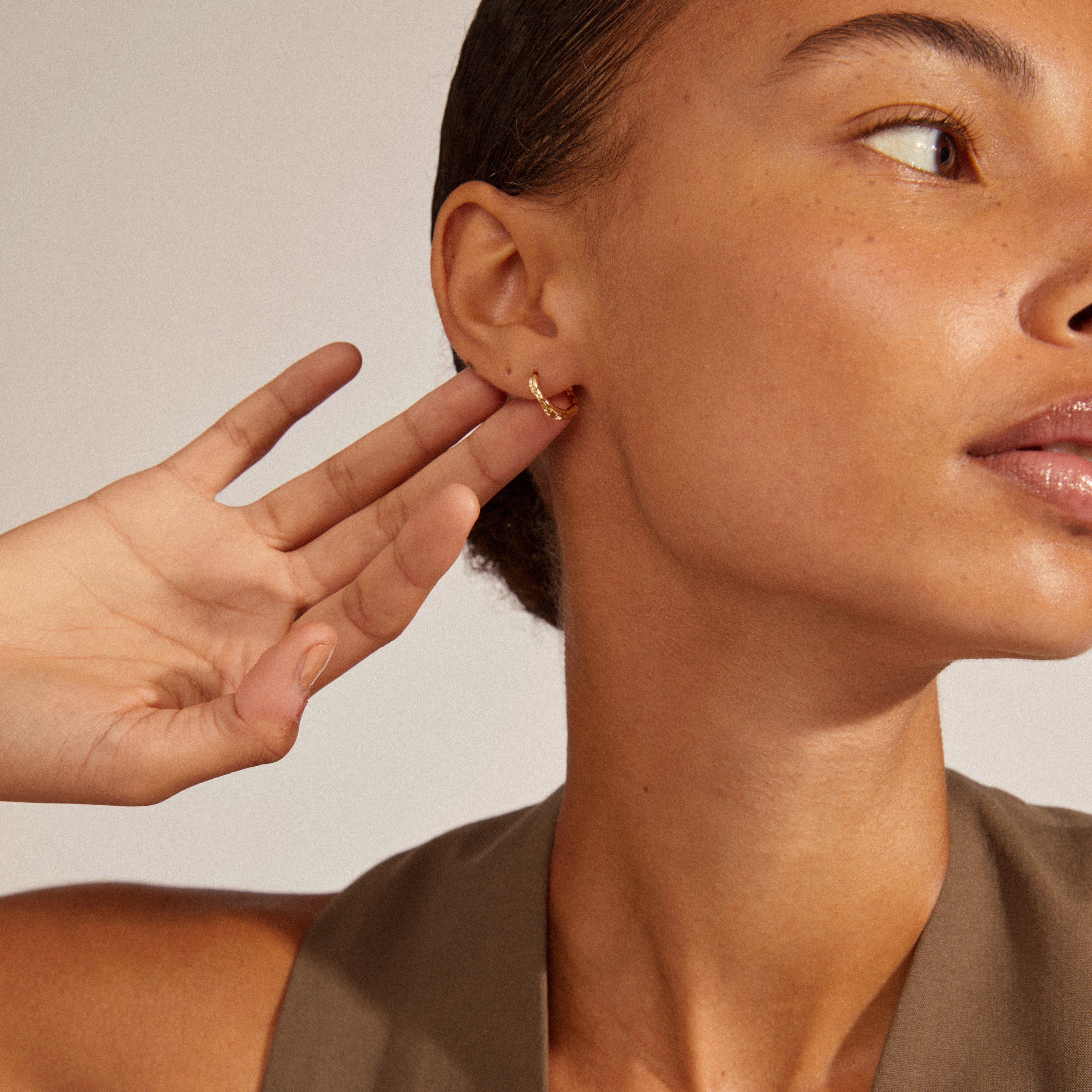 Close-up of a woman wearing EDDY organic-shaped small hoops, gold-plated with a wavy design, capturing their unique handcrafted look.