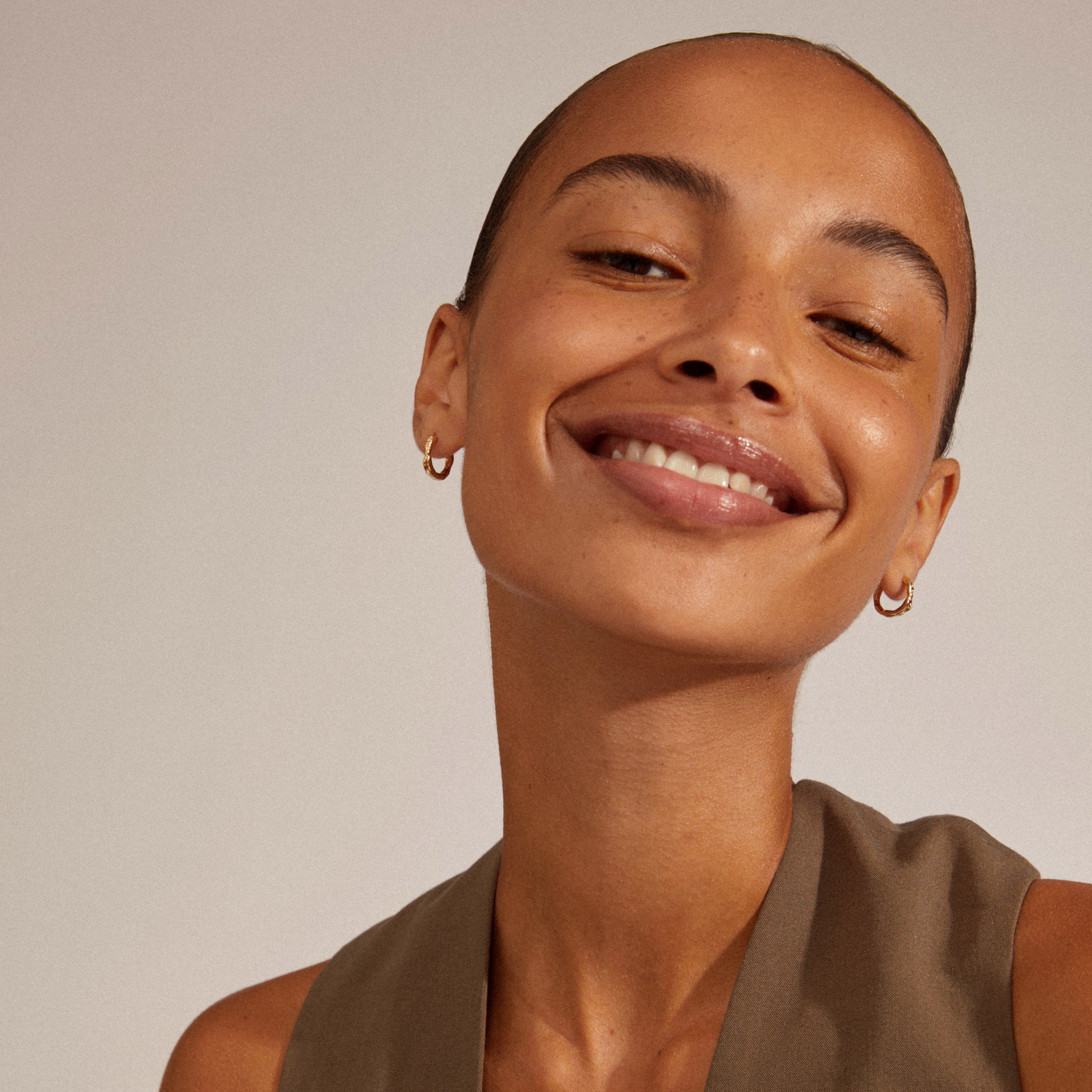 EDDY organic-shaped small hoops, gold-plated, worn by a smiling woman, showcasing their unique, wavy design and easy-to-use click lock.