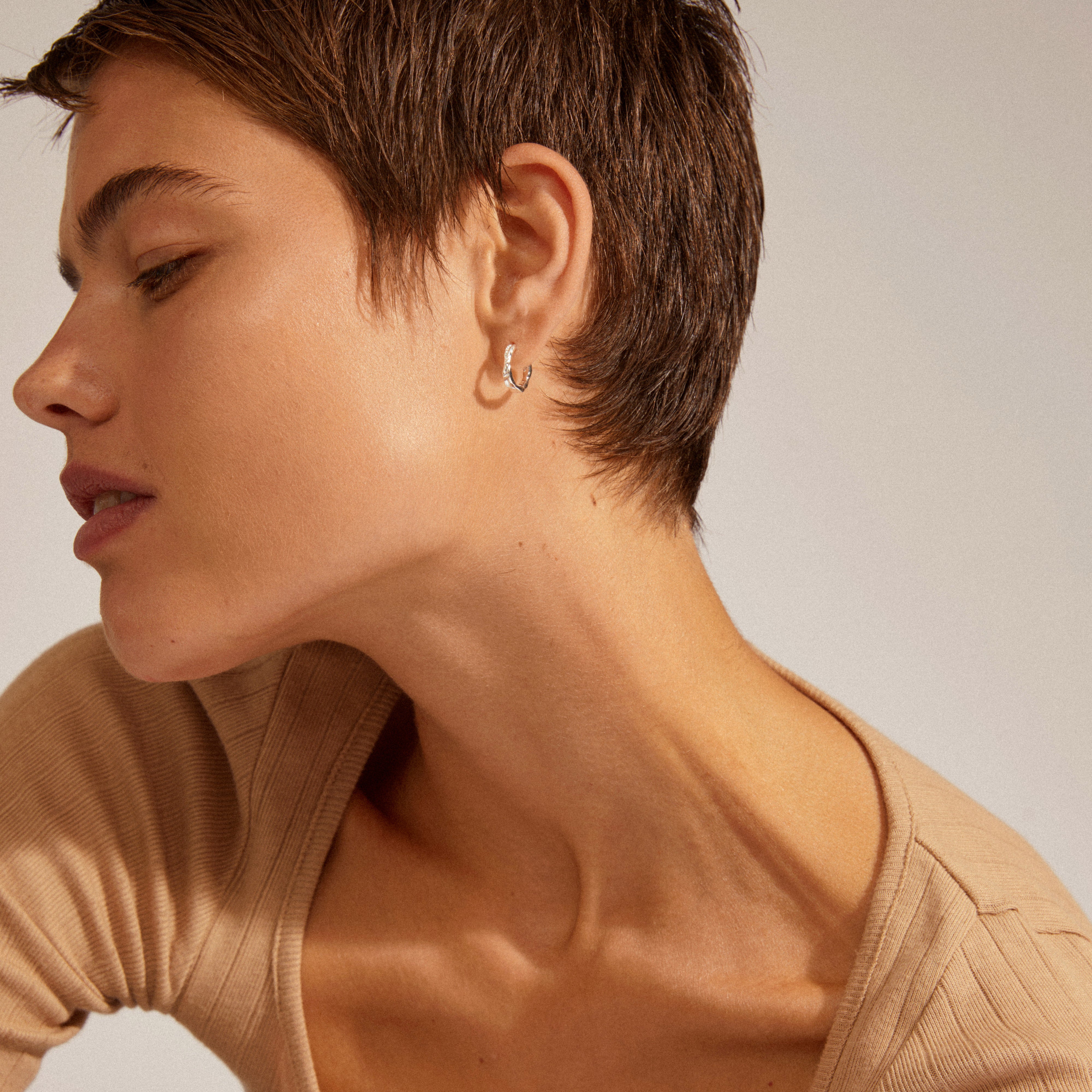 EDDY organic shaped small hoops, silver-plated, showcased on a woman's ear, highlighting their handcrafted, ocean wave-inspired design. Perfect for stylish, everyday wear.